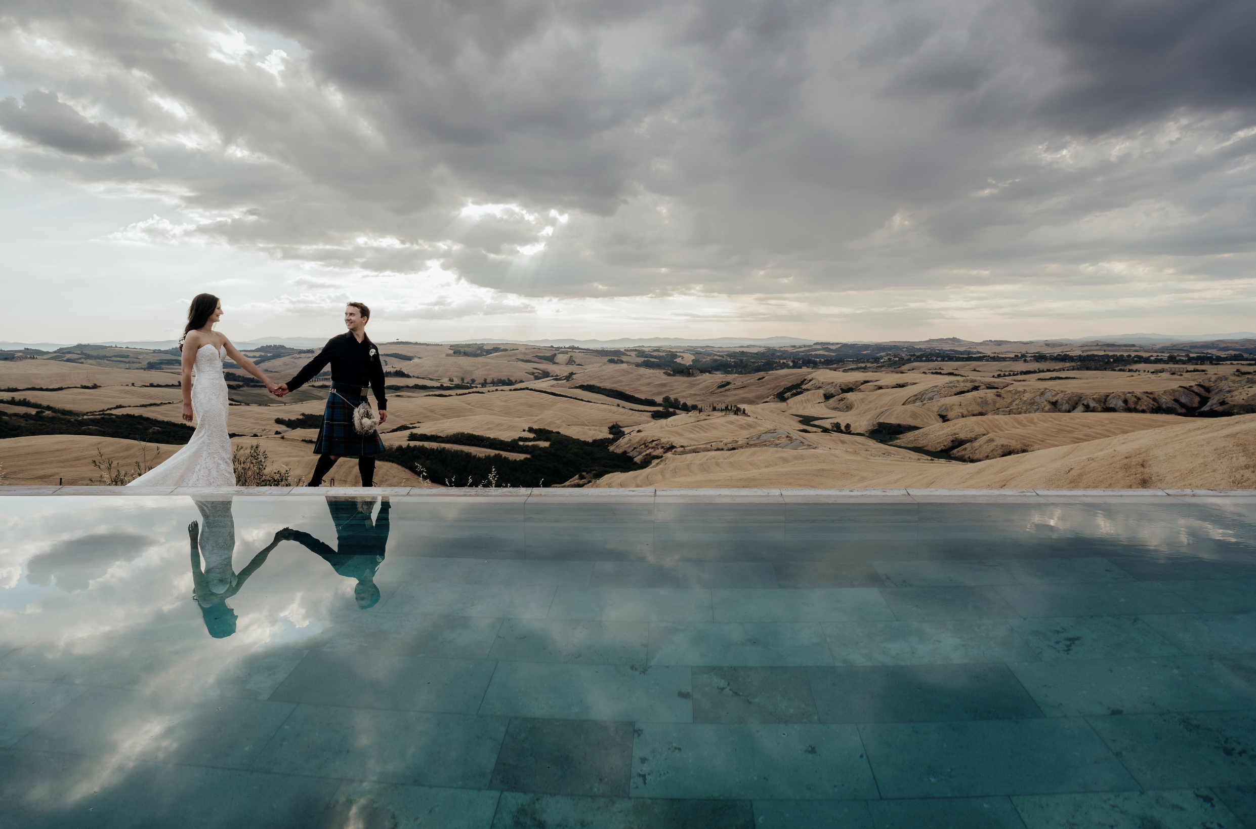 Ellen and Malcolm walking next to a reflective pool overlooking the Tuscany landscape.