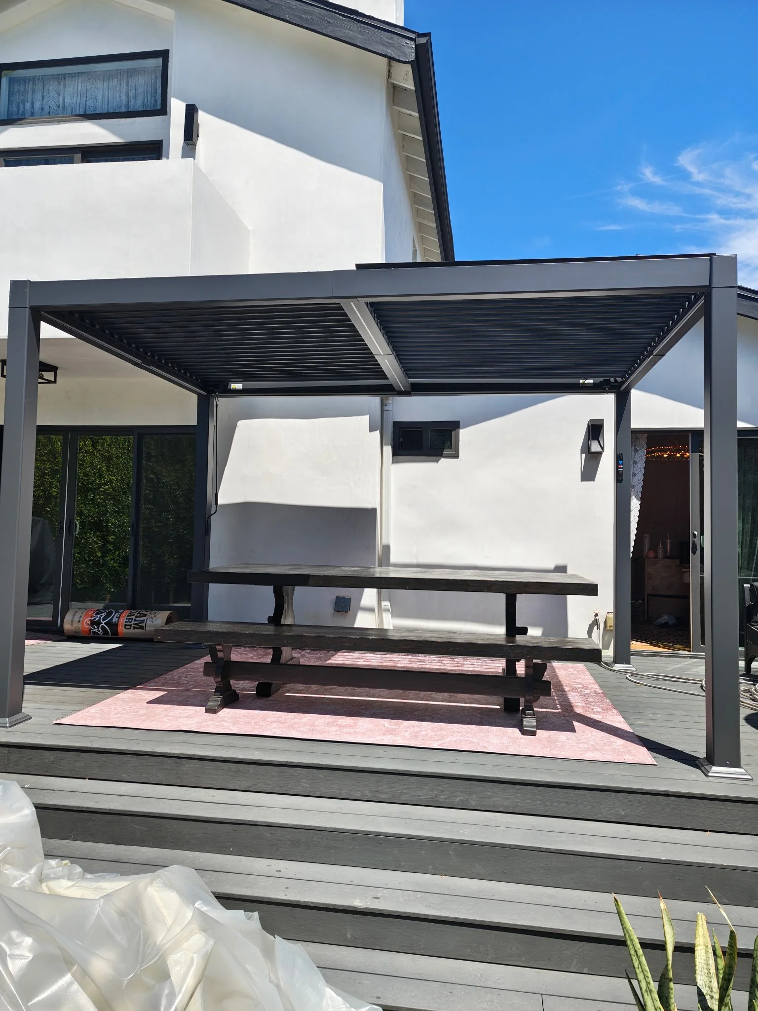Modern patio with a metal pergola, long table, and benches on an outdoor rug.