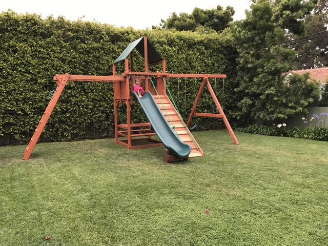 Backyard playset with a slide, small climbing wall, and two swings.