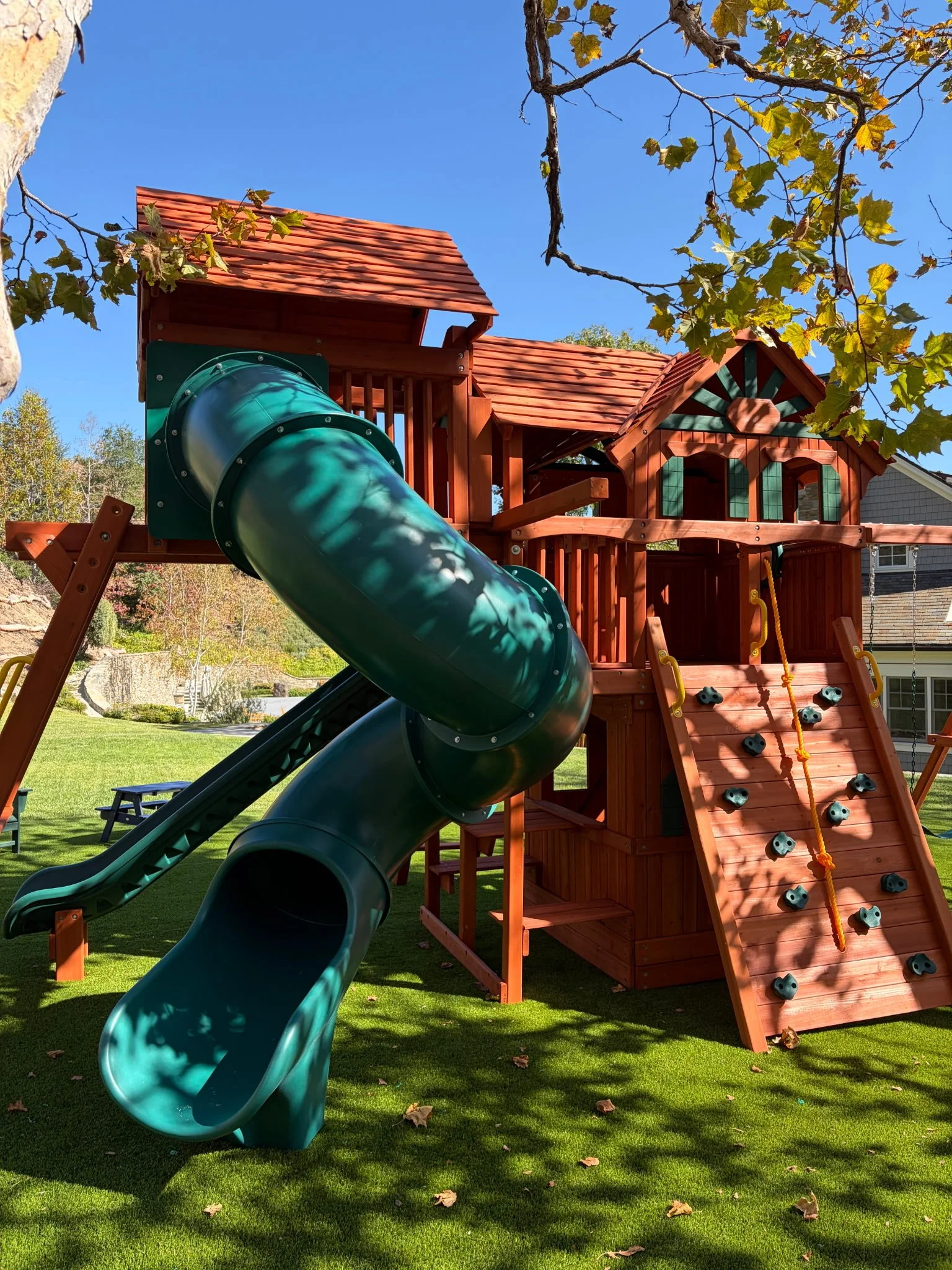 Wooden playset with slides, climbing features, and a grassy yard with trees.