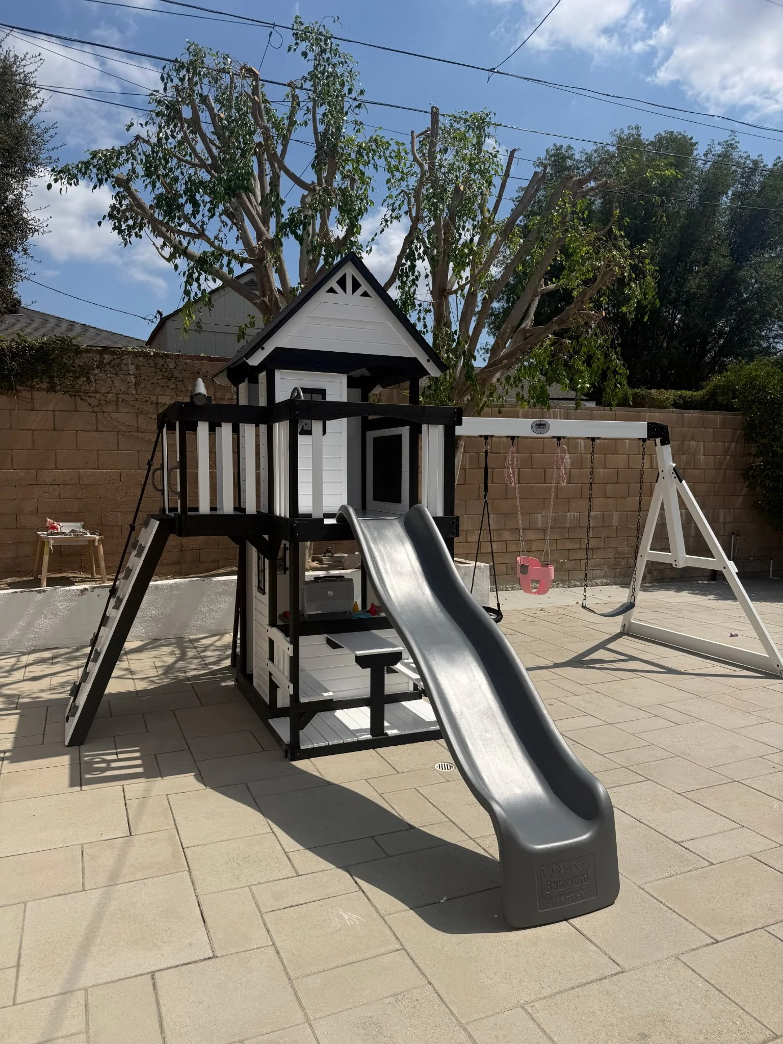 Children’s playhouse with a slide and ladder on a patio near a brick wall.
