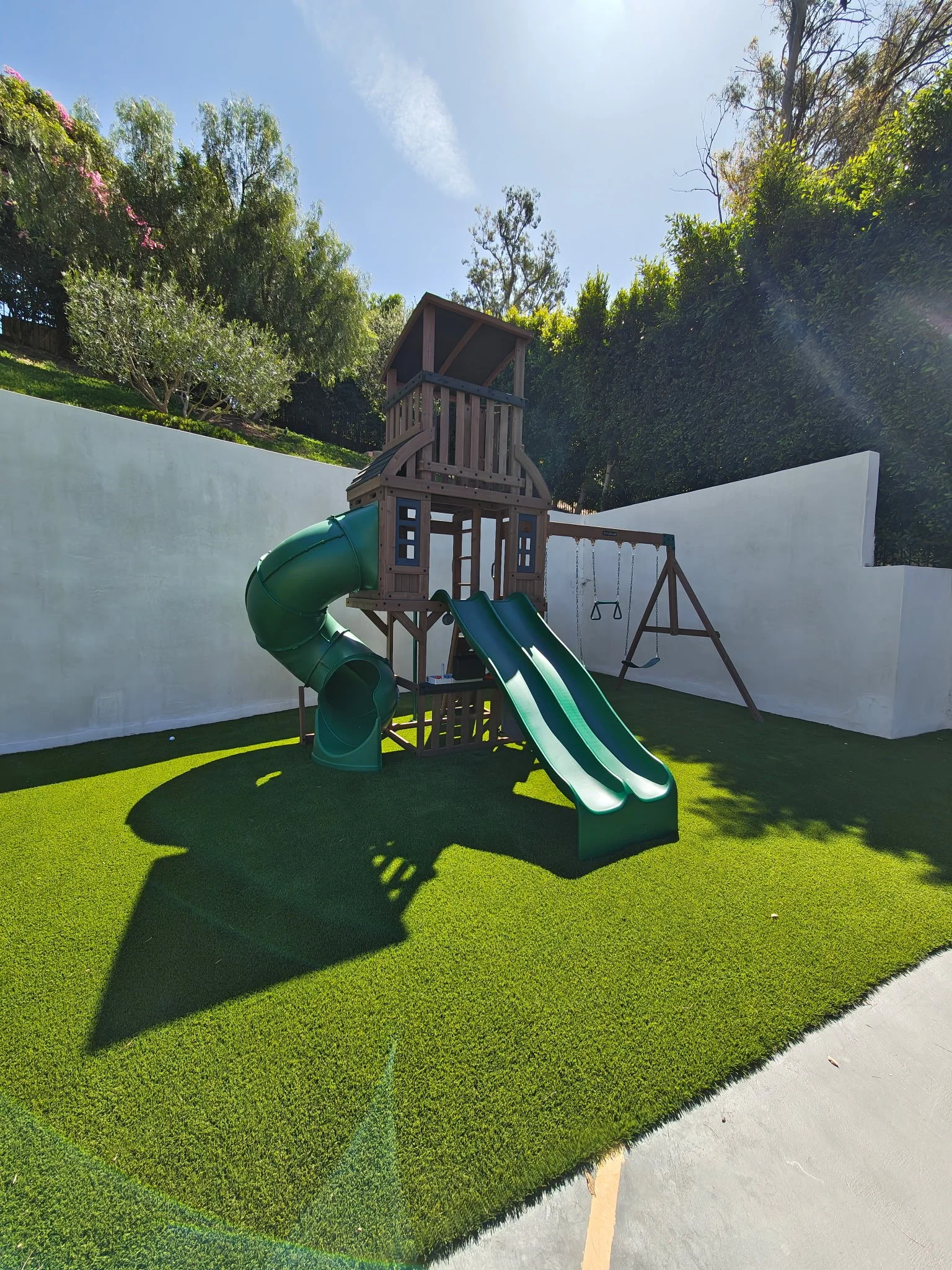 Large wooden playset with a spiral slide, straight slides, and swings on artificial grass.