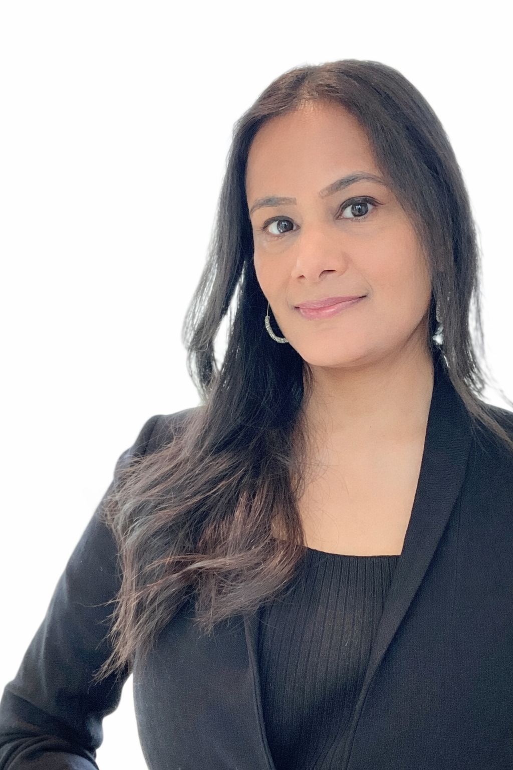 A woman with wavy dark hair, wearing a black blazer and hoop earrings, posing against a white background.
