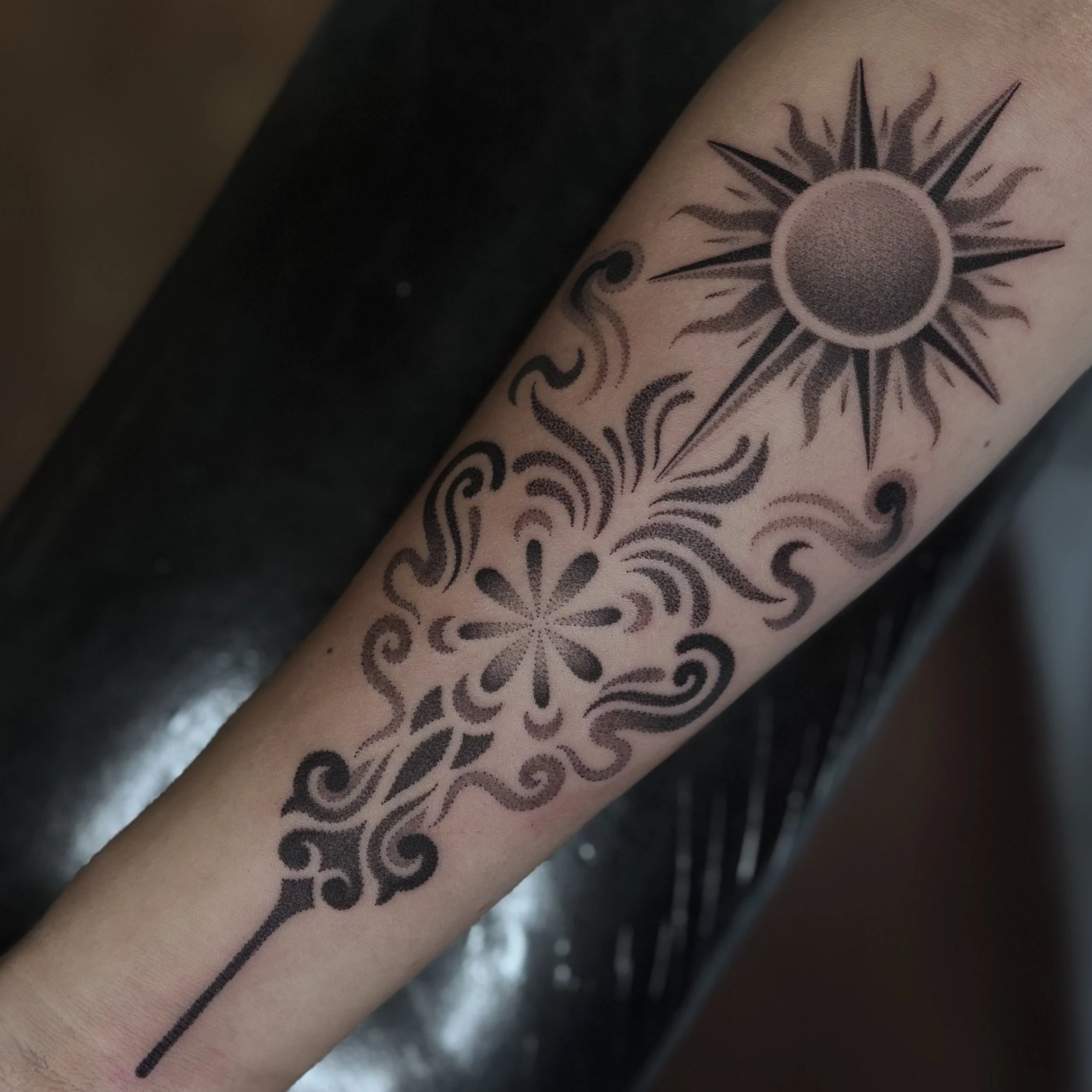 Black and gray ornamental sun and floral tattoo on forearm