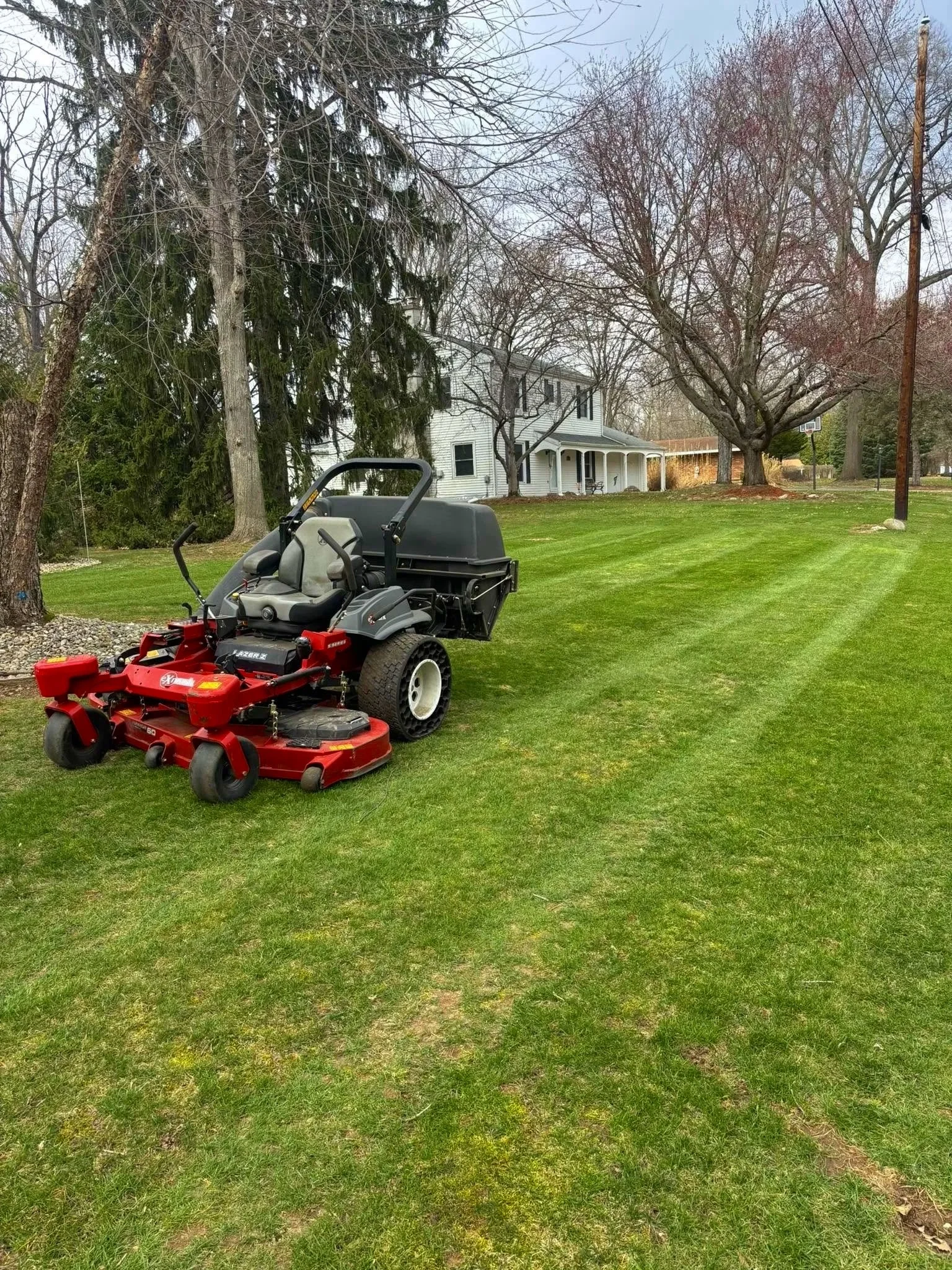 A lawn mower sitting on a green grassy lawn with trees and a house in the background.