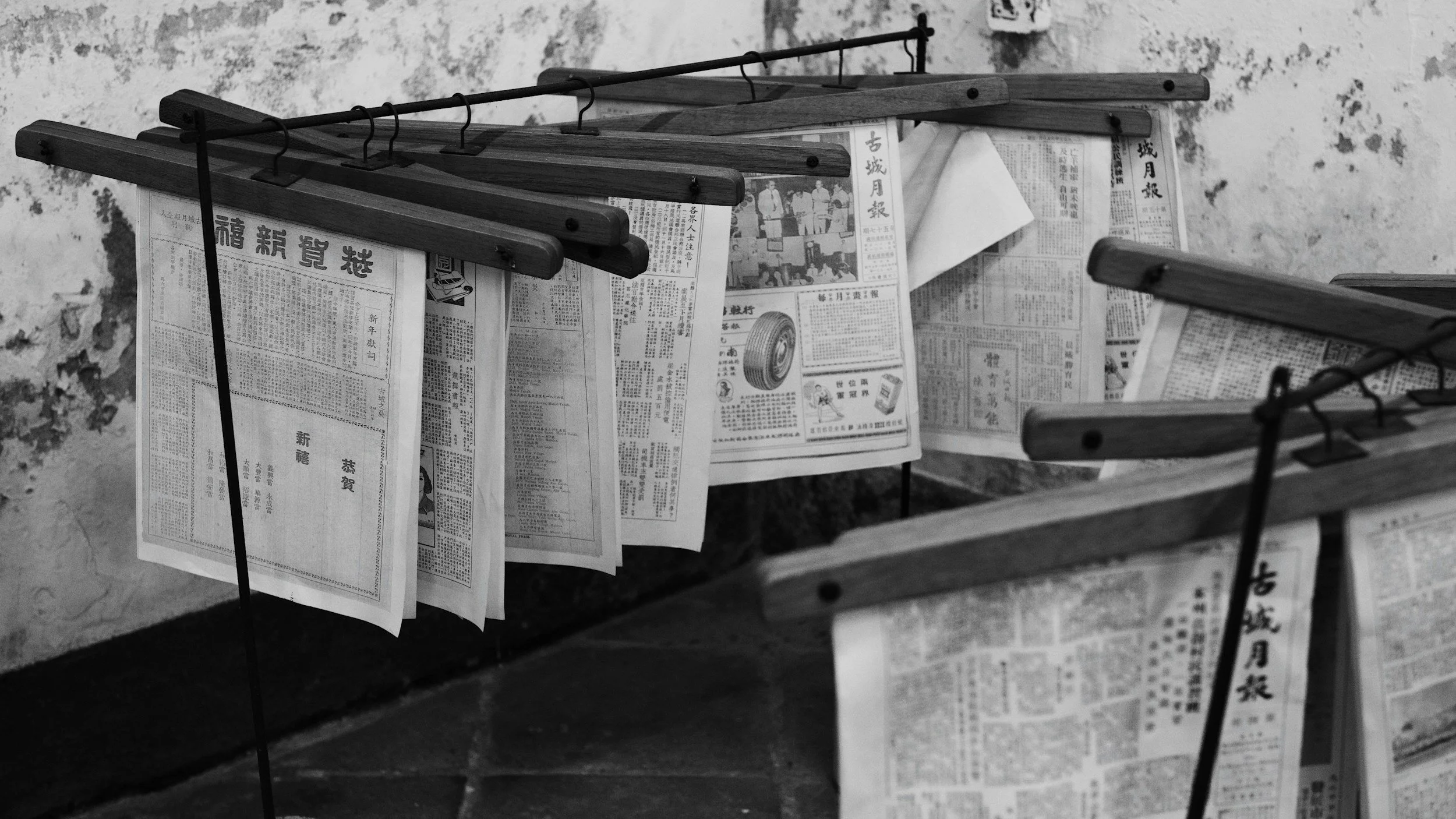 Newspapers hanging on a wooden and metal rack against a textured wall