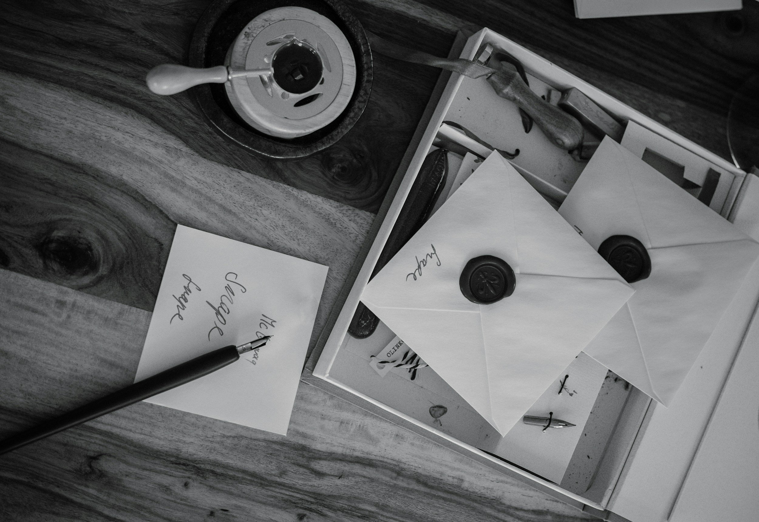 A collection of letters, envelopes with wax seals, a pen, and a letter opener on a wooden surface. One paper has the word 'Thank' written on it.