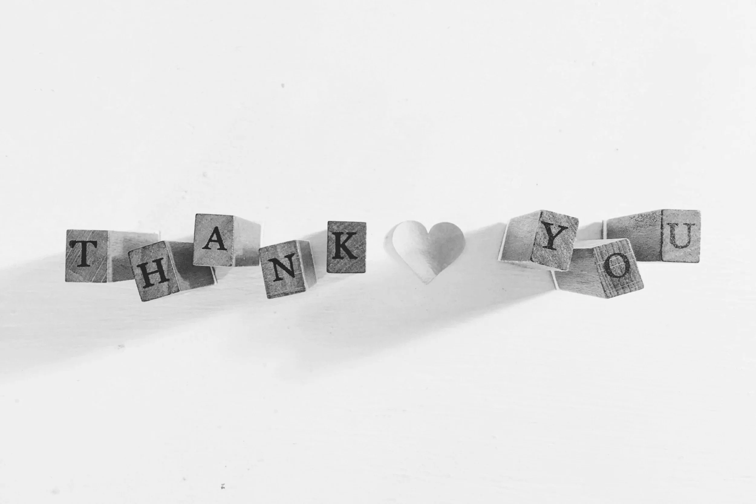 Black and white photograph of wooden blocks spelling out 'THANK YOU' with a heart shape between 'N' and 'Y' on a plain background.