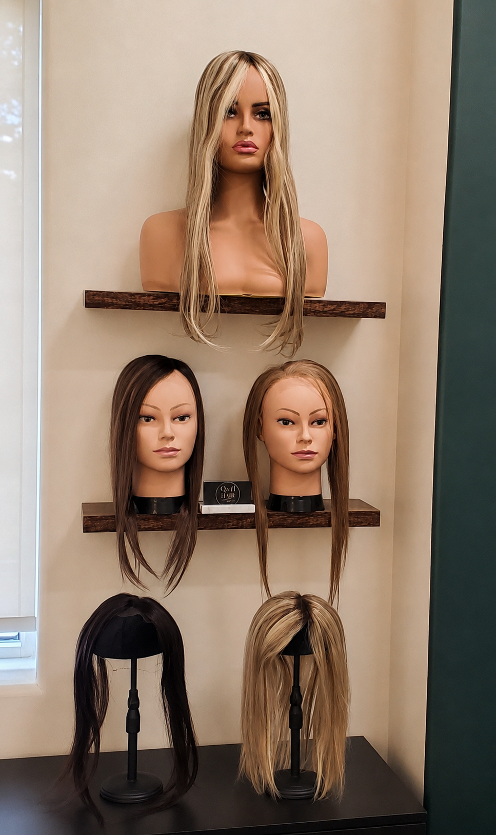 Several wigs and hair toppers displayed on mannequin heads