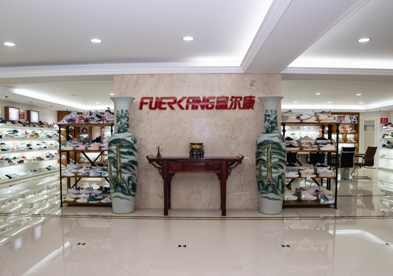 Interior of a shoe store with display shelves filled with shoes on both sides, a tiled floor, and a decorative wall with the sign 'FUERKANG' in red letters and Chinese characters, flanked by two tall decorative vases.