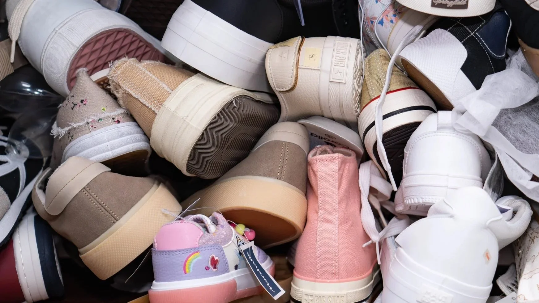 Pile of various sneakers and shoes in different colors and styles, including high-tops, slip-ons, and Velcro sneakers.