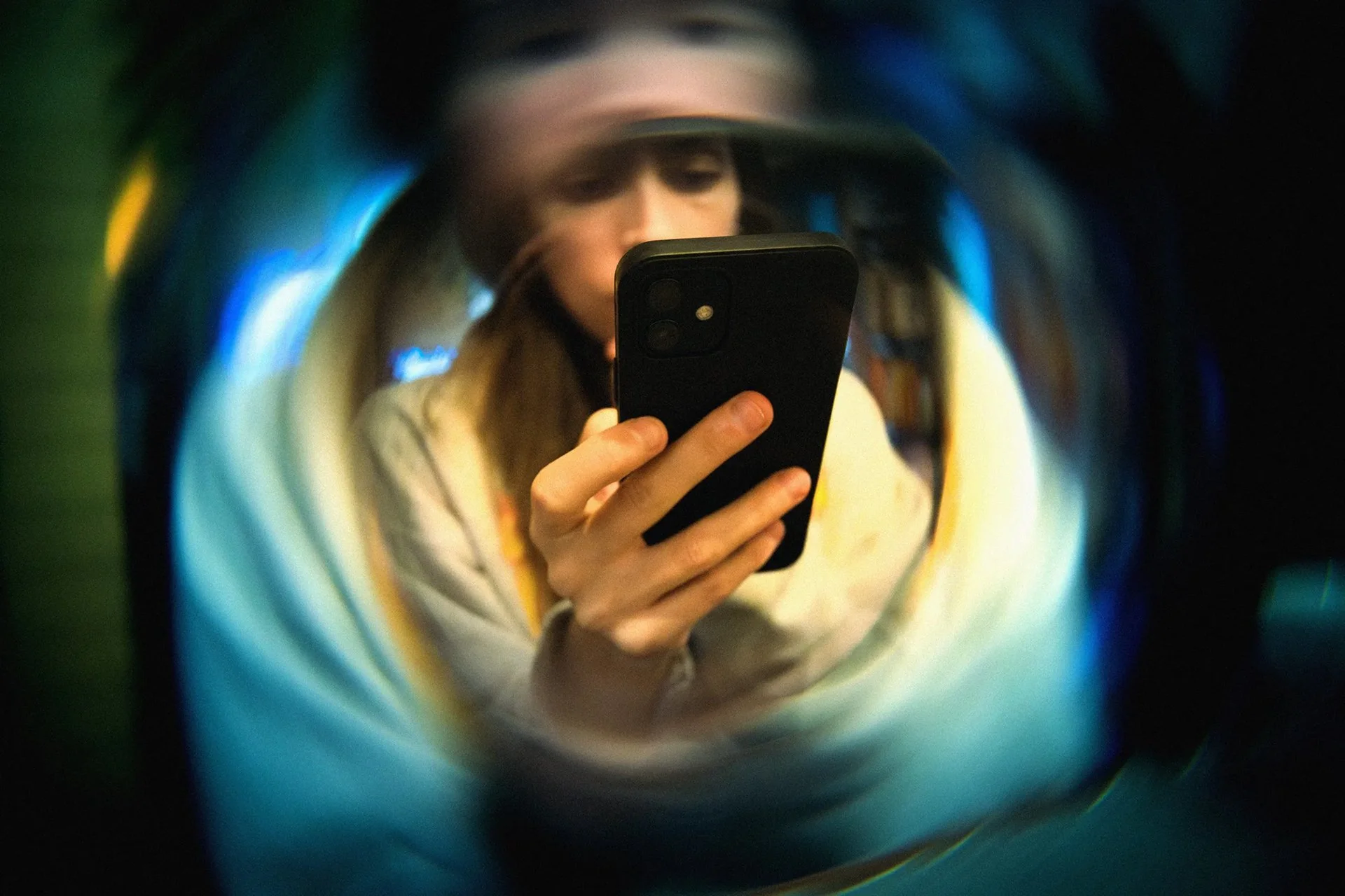 A person holding and looking at a smartphone through a colorful, swirling tunnel-like structure with blue, yellow, and green hues that expresses stress, drama and pressure.