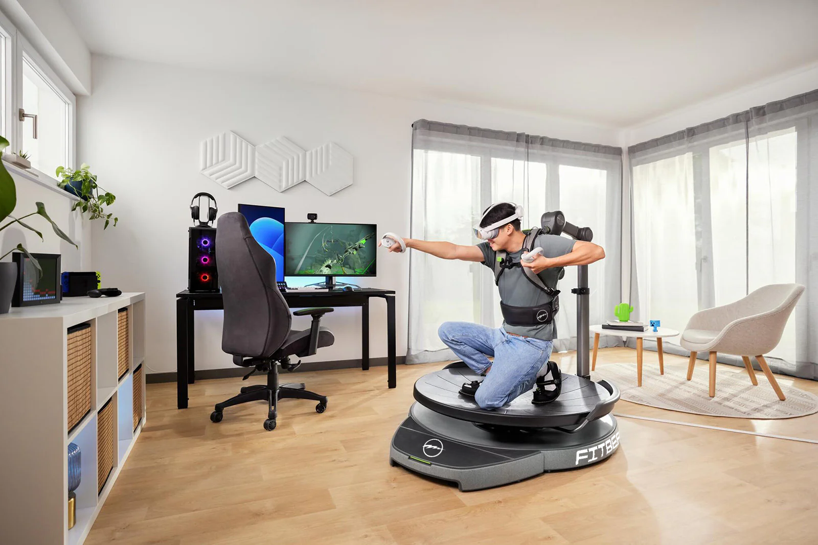 A person is using a virtual reality setup on a rotating platform in a modern living room with computer stations, a chair, and sheer window curtains. The kneel on one knee and point their right arm out while holding controllers and wearing VR headset.