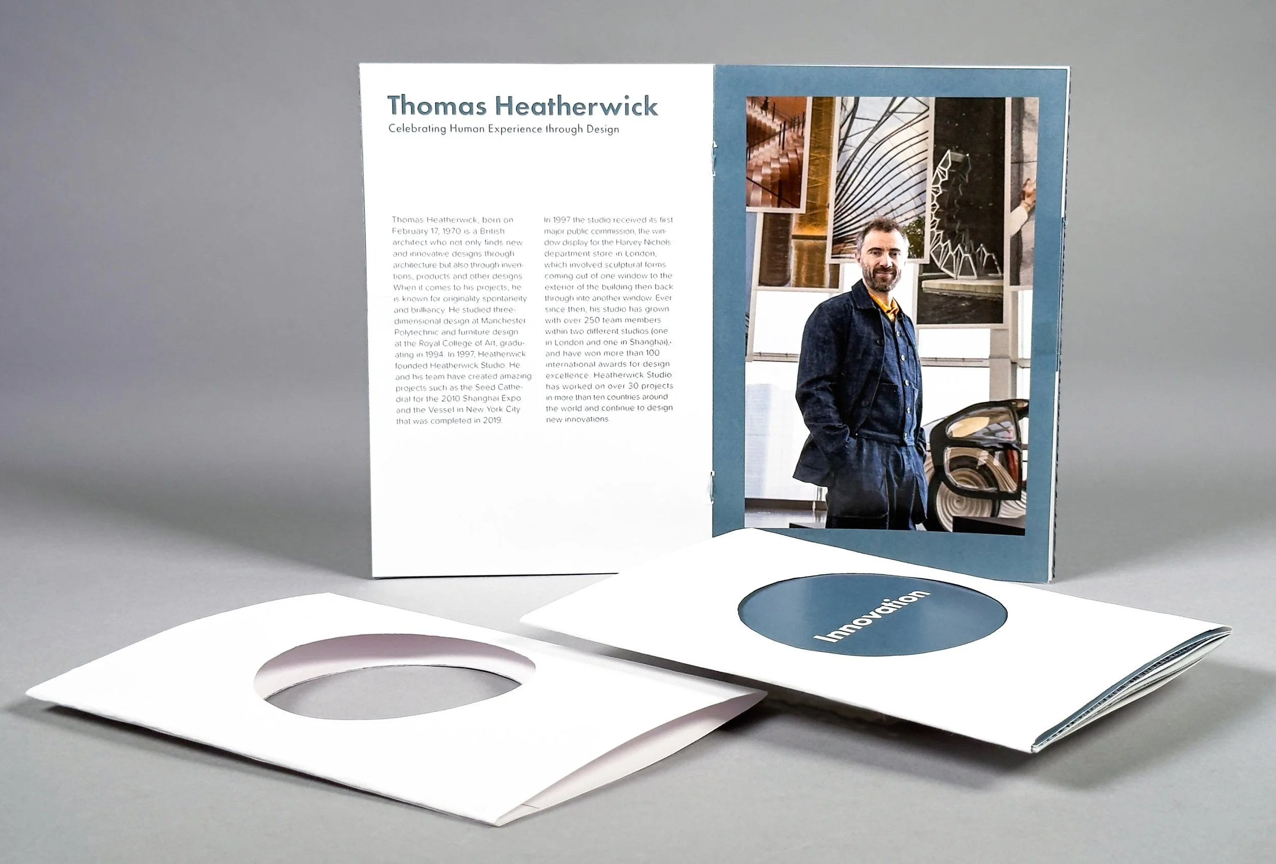 Open brochure featuring information on Thomas Heatherwick, with images of architectural structures, as circular paper cutouts lie below with the word "Innovation" on a blue background.