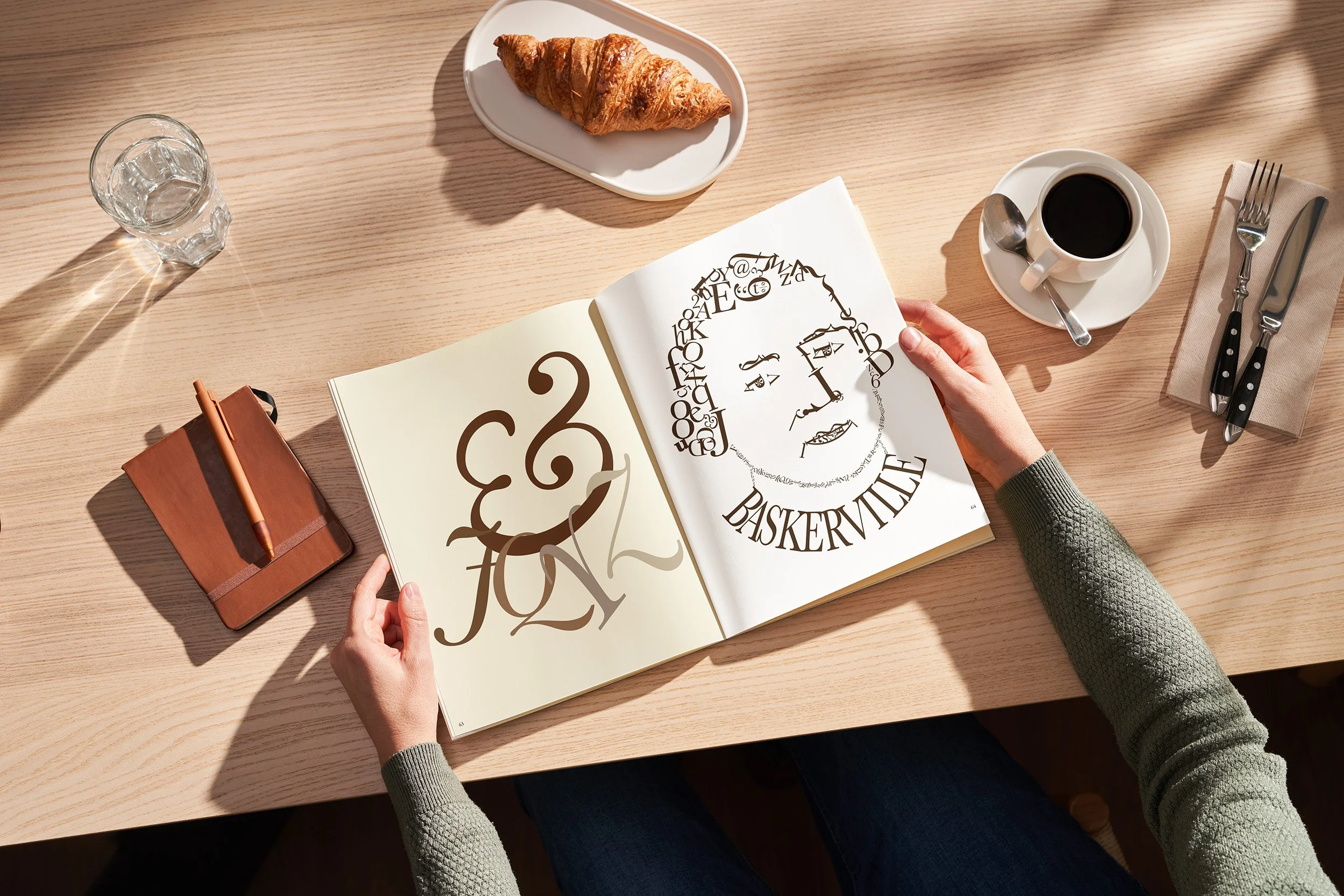 A person at a cafe, holding an open magazine. On the left is the playful imagery of letters hanging off an ampersand while the right page depicts the face of John Baskerville made up of only letters, numbers and symbols from the Baskerville typeface.