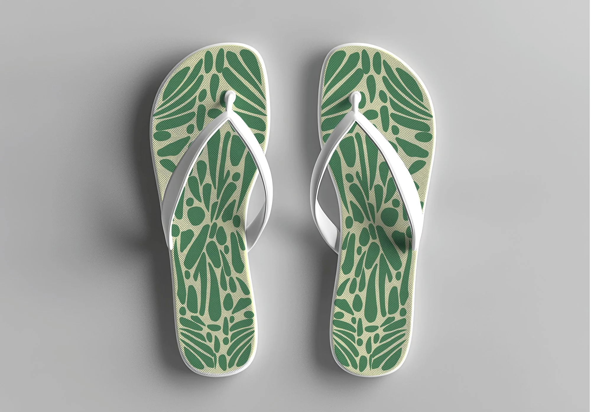 Pair of flip-flops with green and beige leaf pattern, white straps, placed on a gray surface.