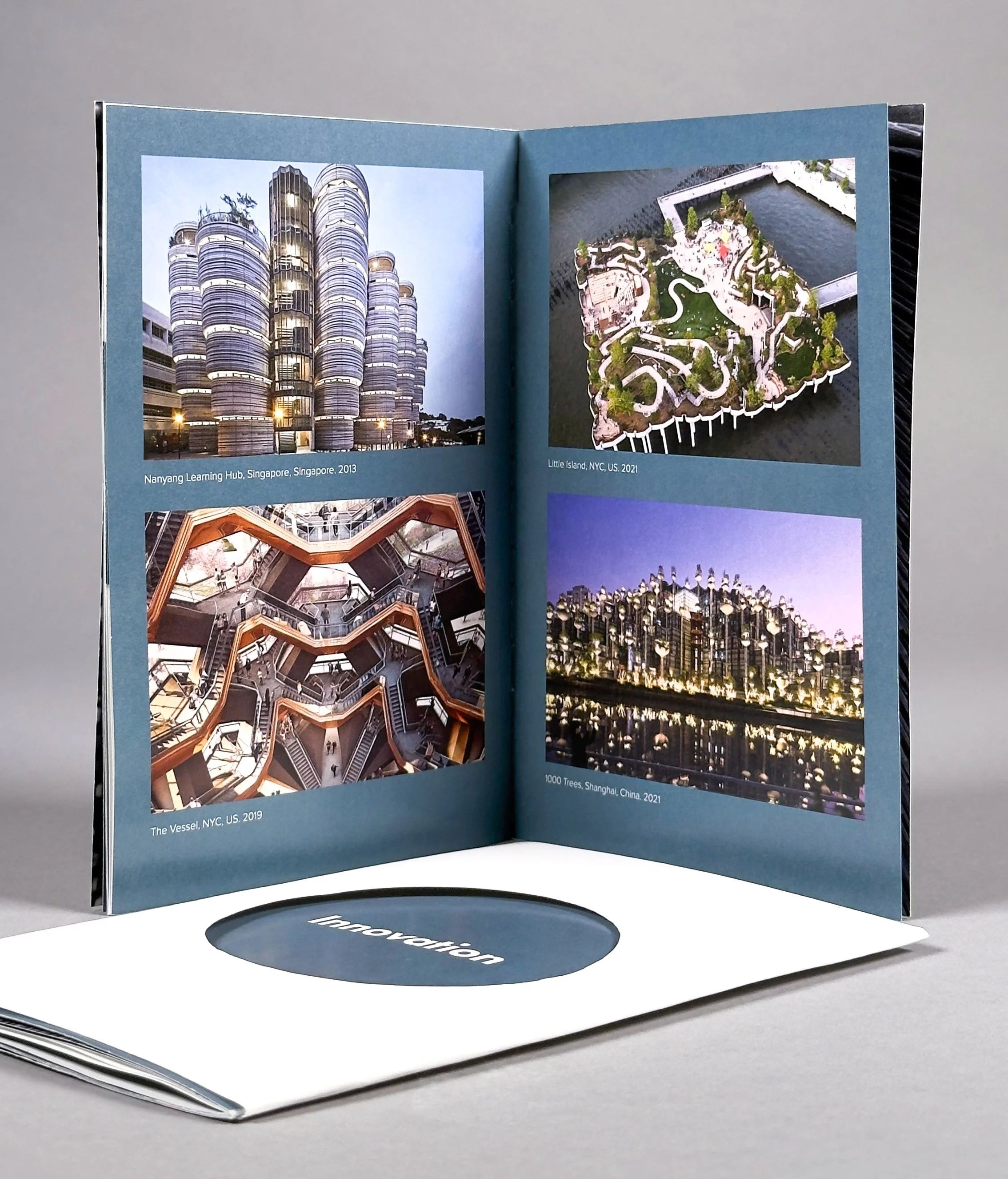 Open booklet showing images of architectural projects, including a building in Singapore, a miniature landscape in NYC, and a structure in Shanghai with a reflective water feature.