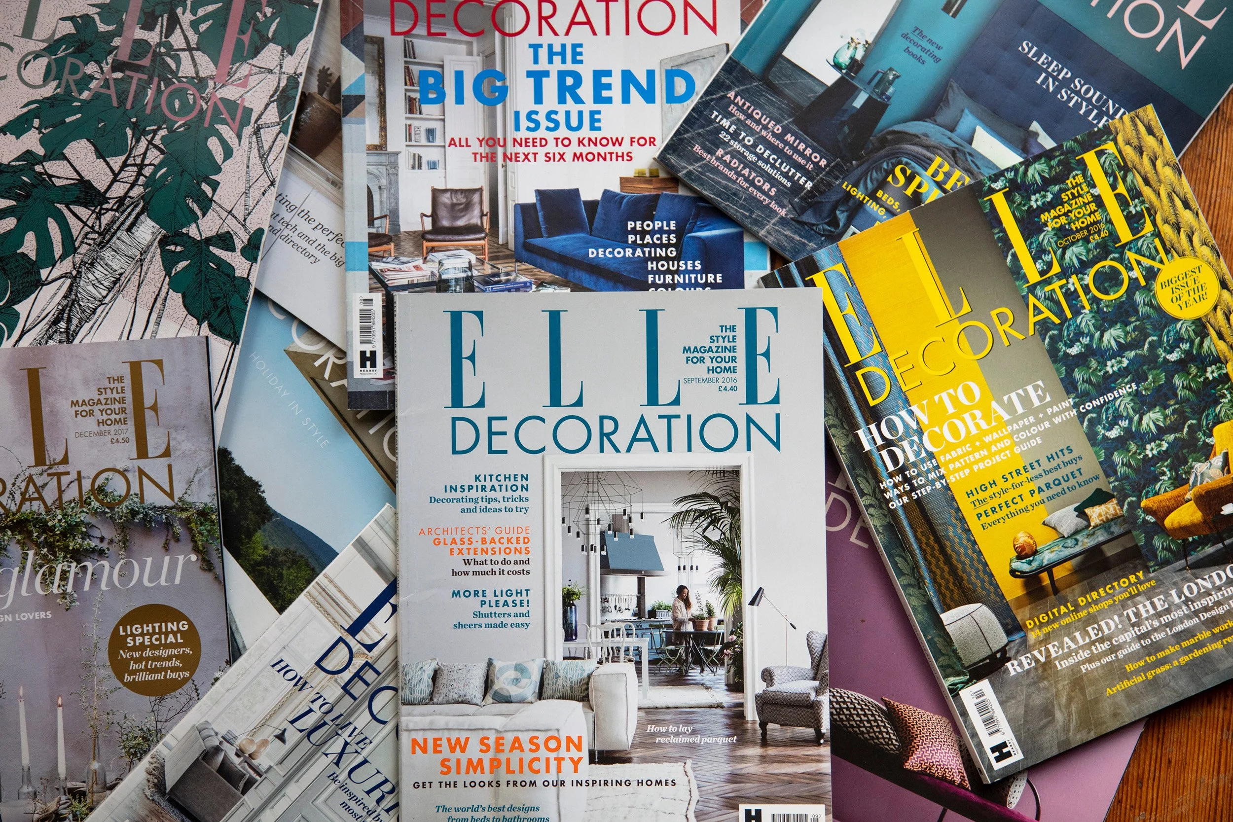 A collection of interior design and home decor magazines spread out on a wooden surface, featuring covers about decoration trends, styling tips, and home inspiration.