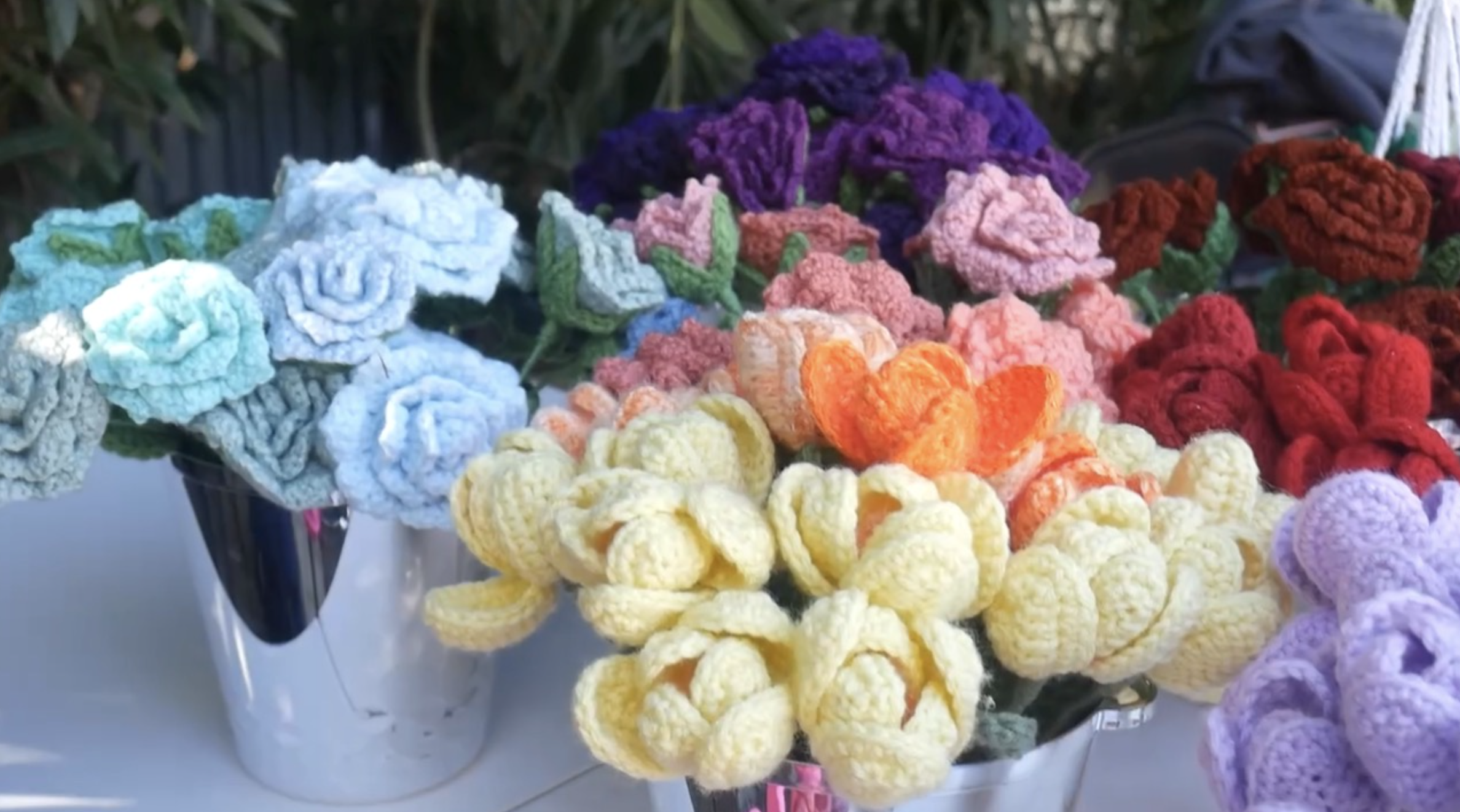 Display of multicolored crocheted roses and tulips in baskets on a table.