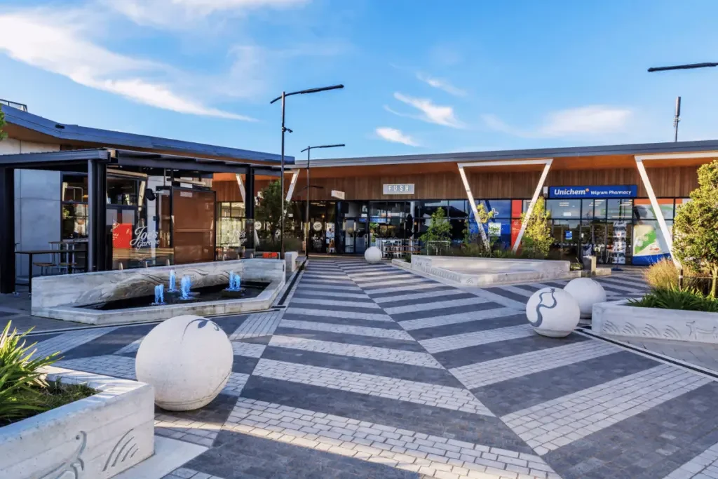 The Landing Wigram town centre in Christchurch featuring the central pedestrian plaza, landscaped seating areas, Silky Otter cinema entrance, cafés, restaurants and modern outdoor public spaces on a sunny day.