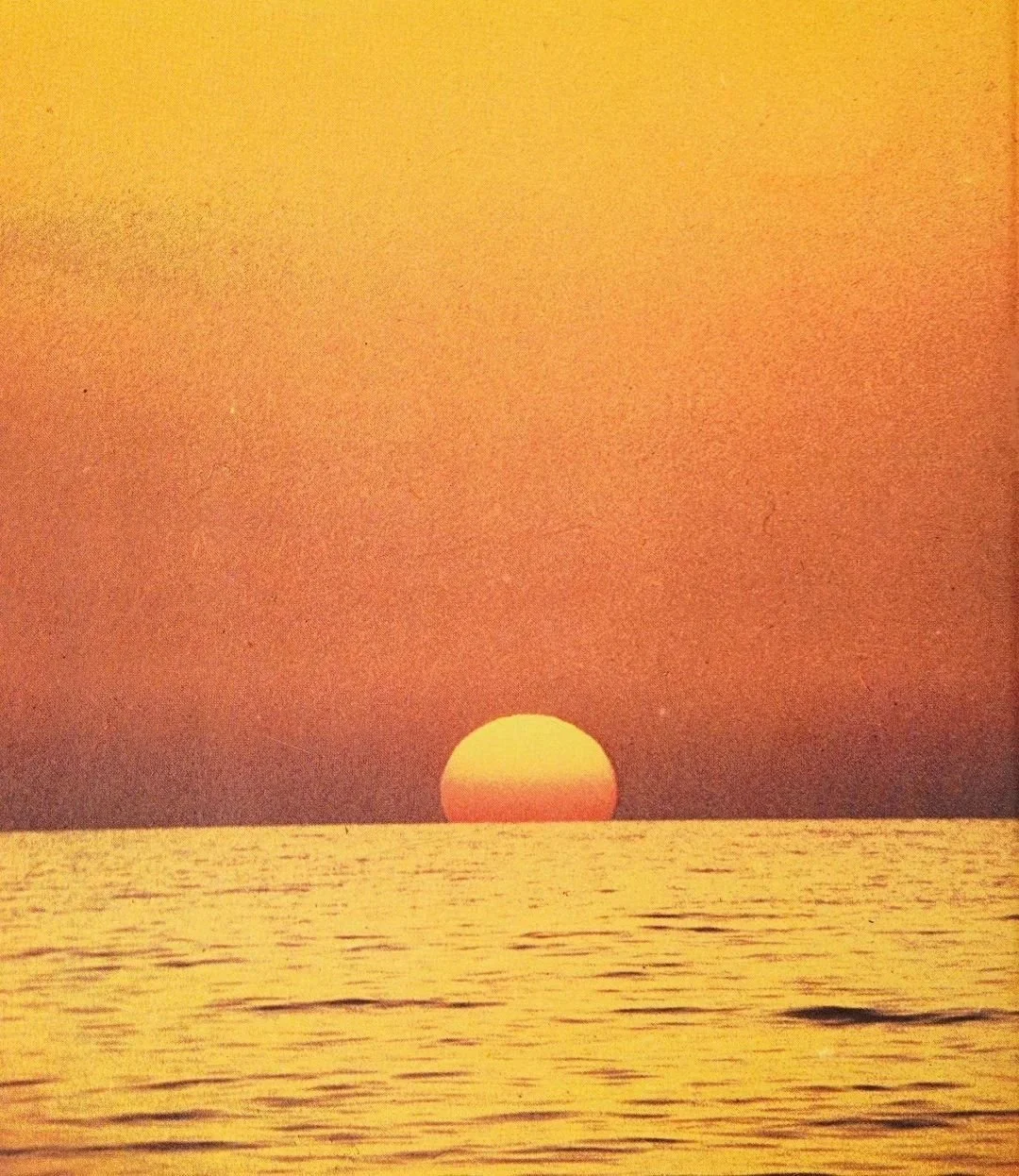 Sun setting over the ocean with a warm orange sky.