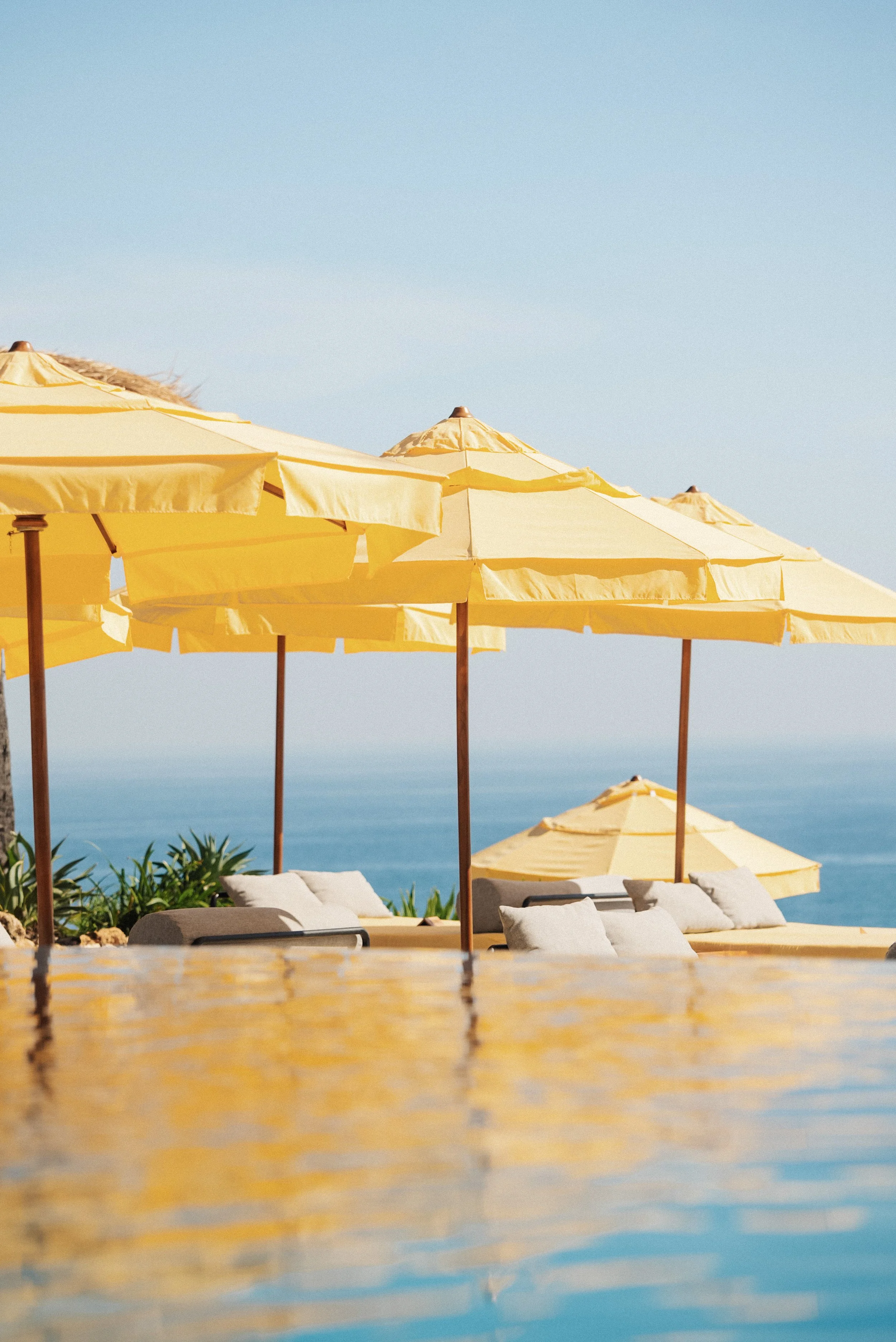 Yellow beach umbrellas and lounge chairs on a sunny day with blue sky and ocean in the background.