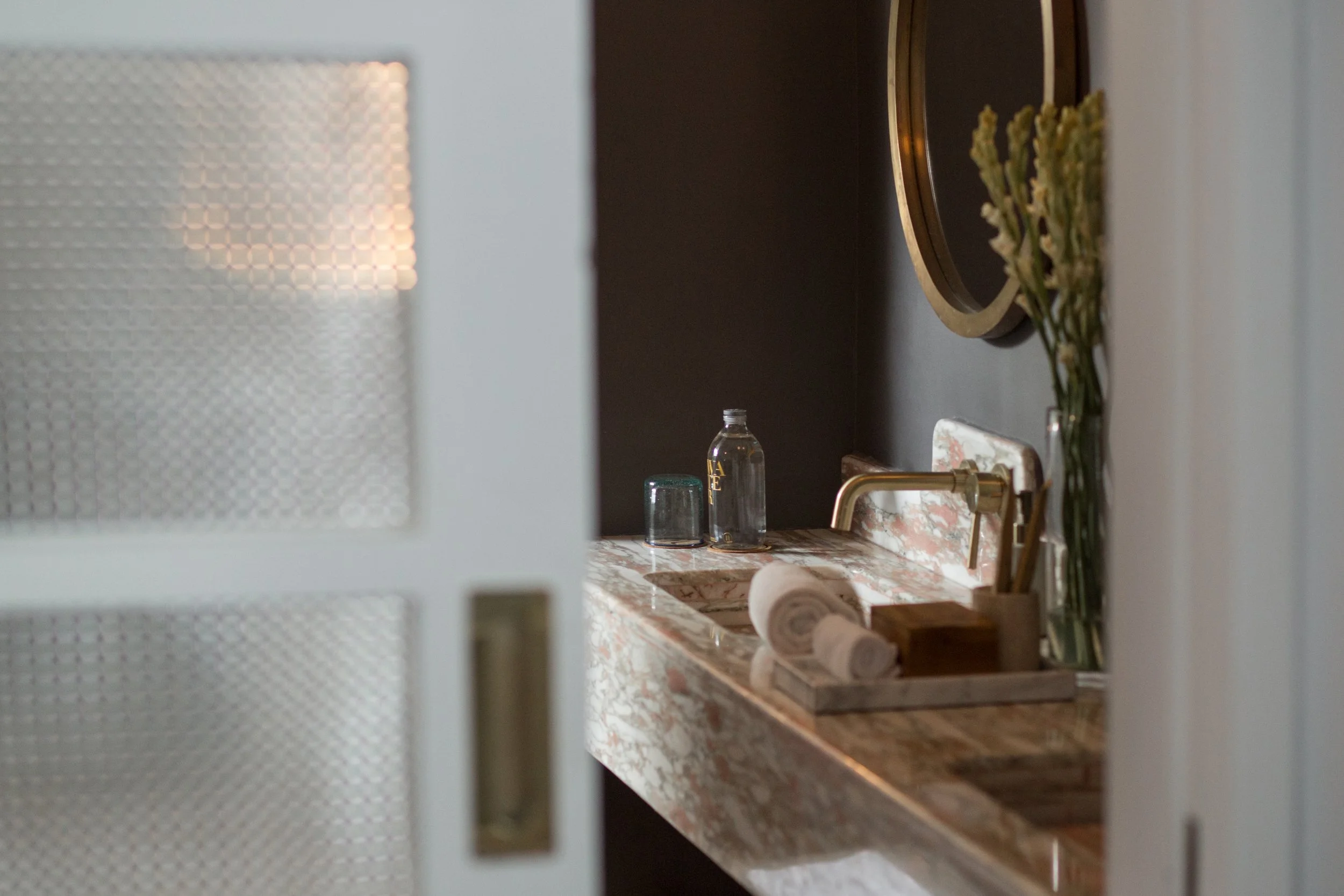 A view of a kitchen area seen through a lattice door, showing a marble countertop, a faucet, and a vase with flowers.