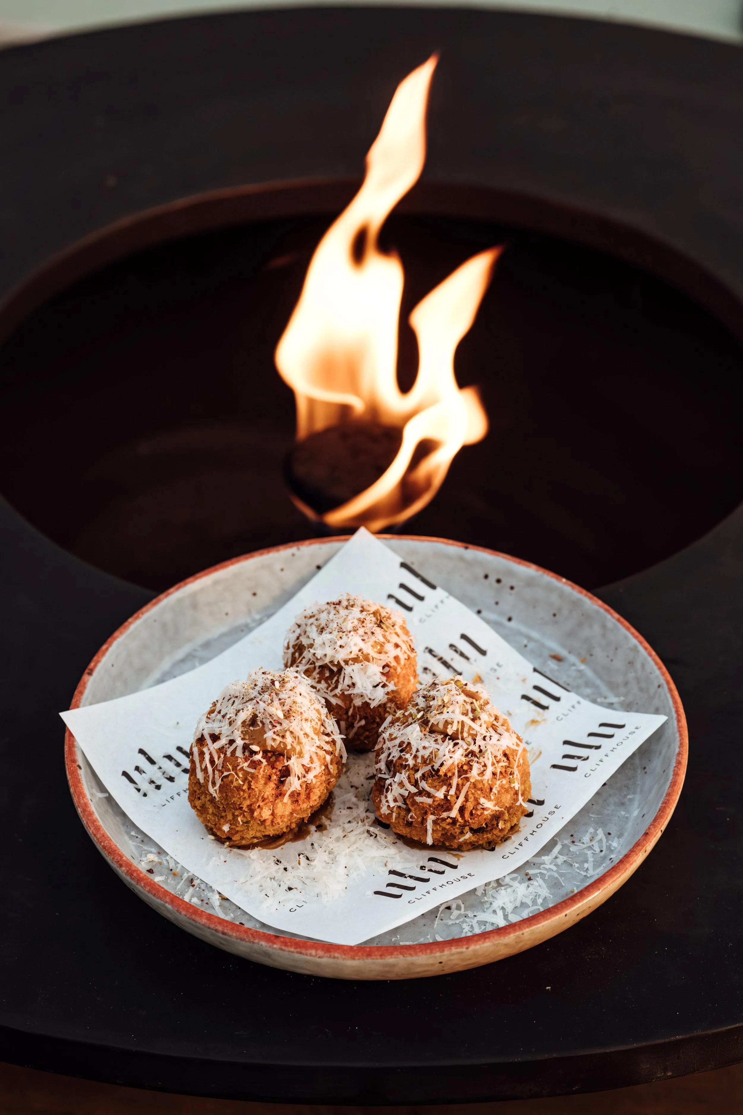 A bowl of four coconut-covered confections topped with shredded coconut, with a flame burning above them.