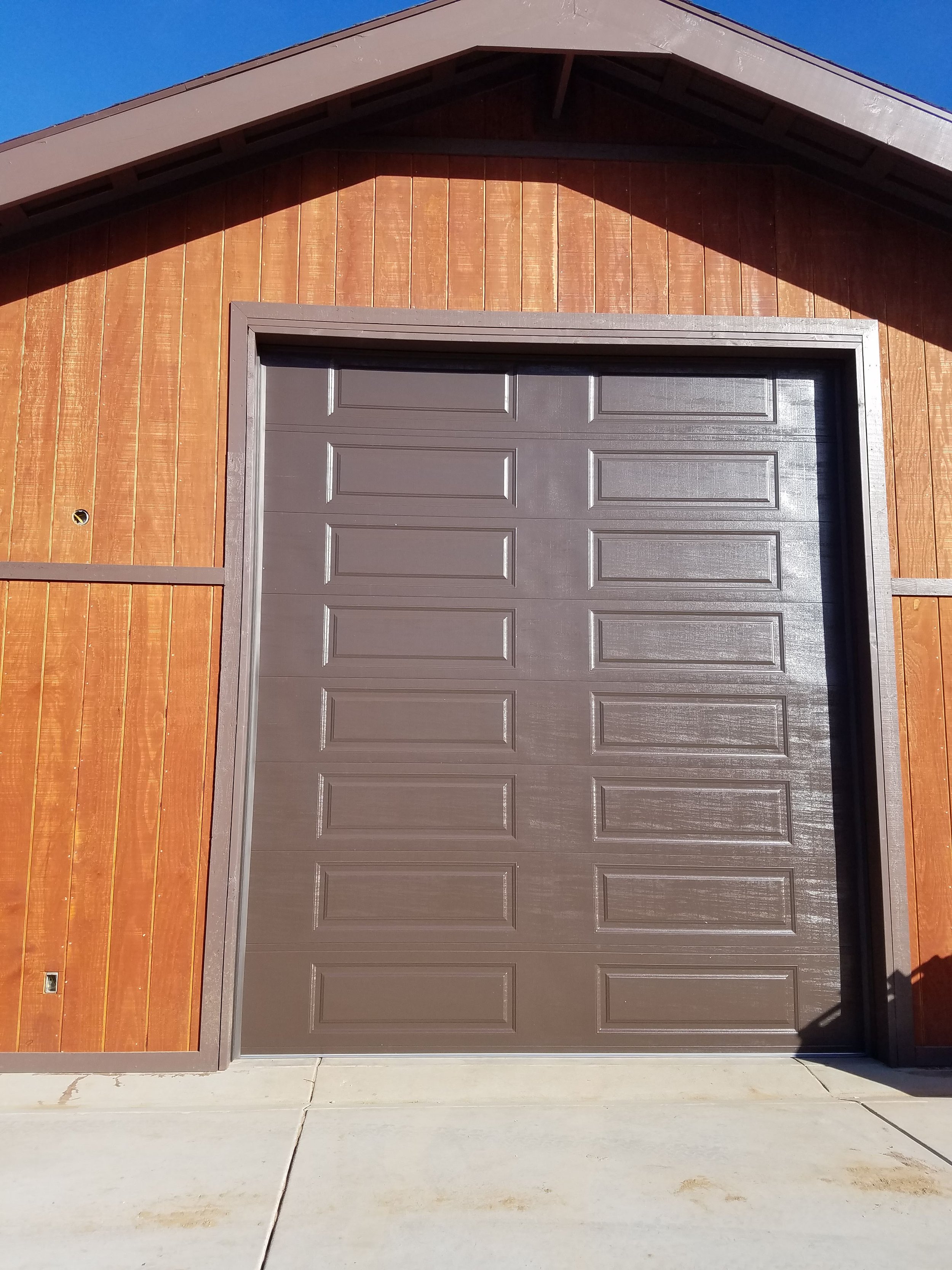 A garage door on a house with wooden siding and a brown roof, under a clear blue sky.