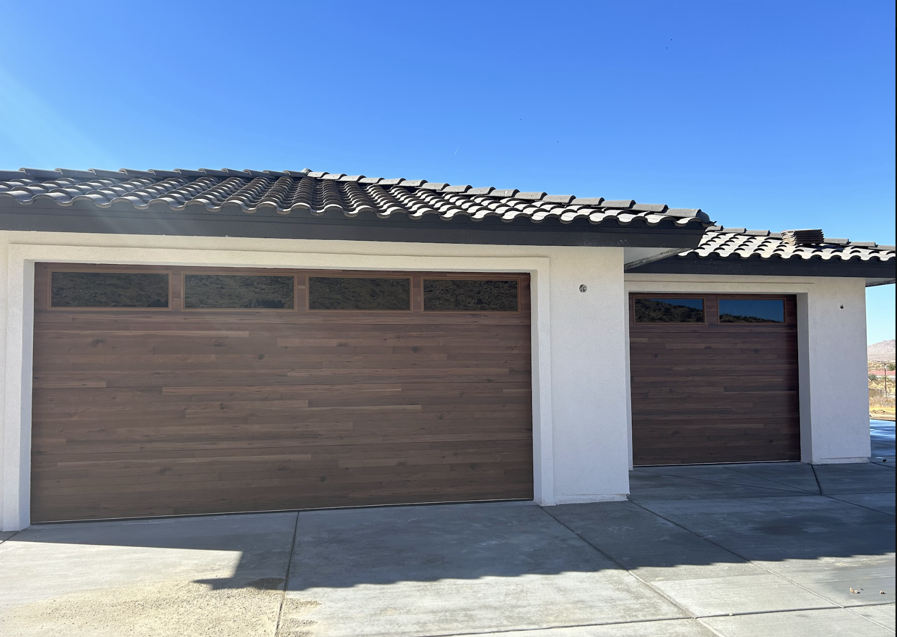 Front view of a house with two wooden garage doors, white walls, and a tiled roof under a clear blue sky.