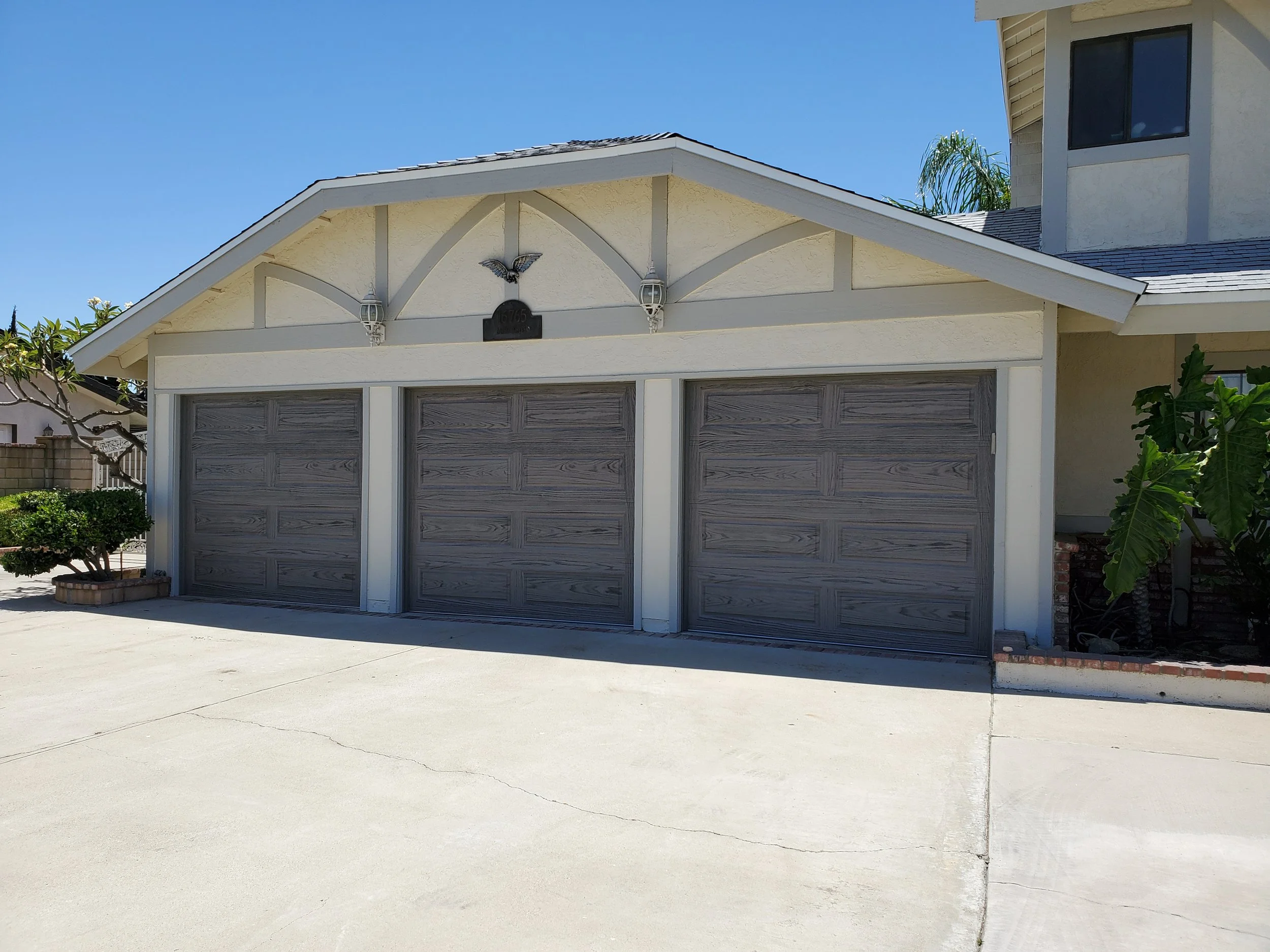Front view of a house with a garage, white walls, a gable roof, a metal sculpture of a bird above the garage, and plants beside the driveway.