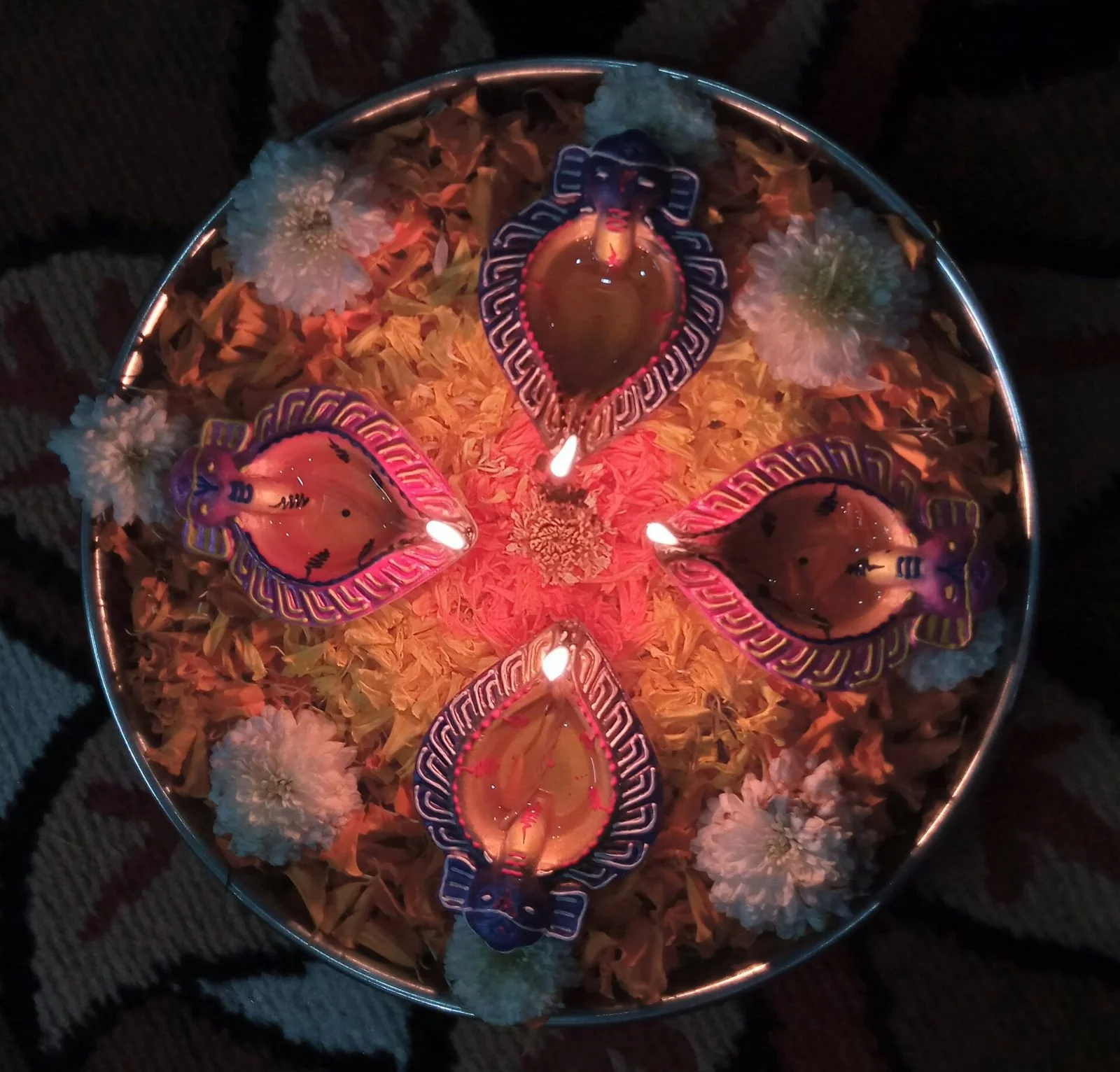 Lit clay diyas arranged on a plate of marigold petals for Diwali, the festival of lights