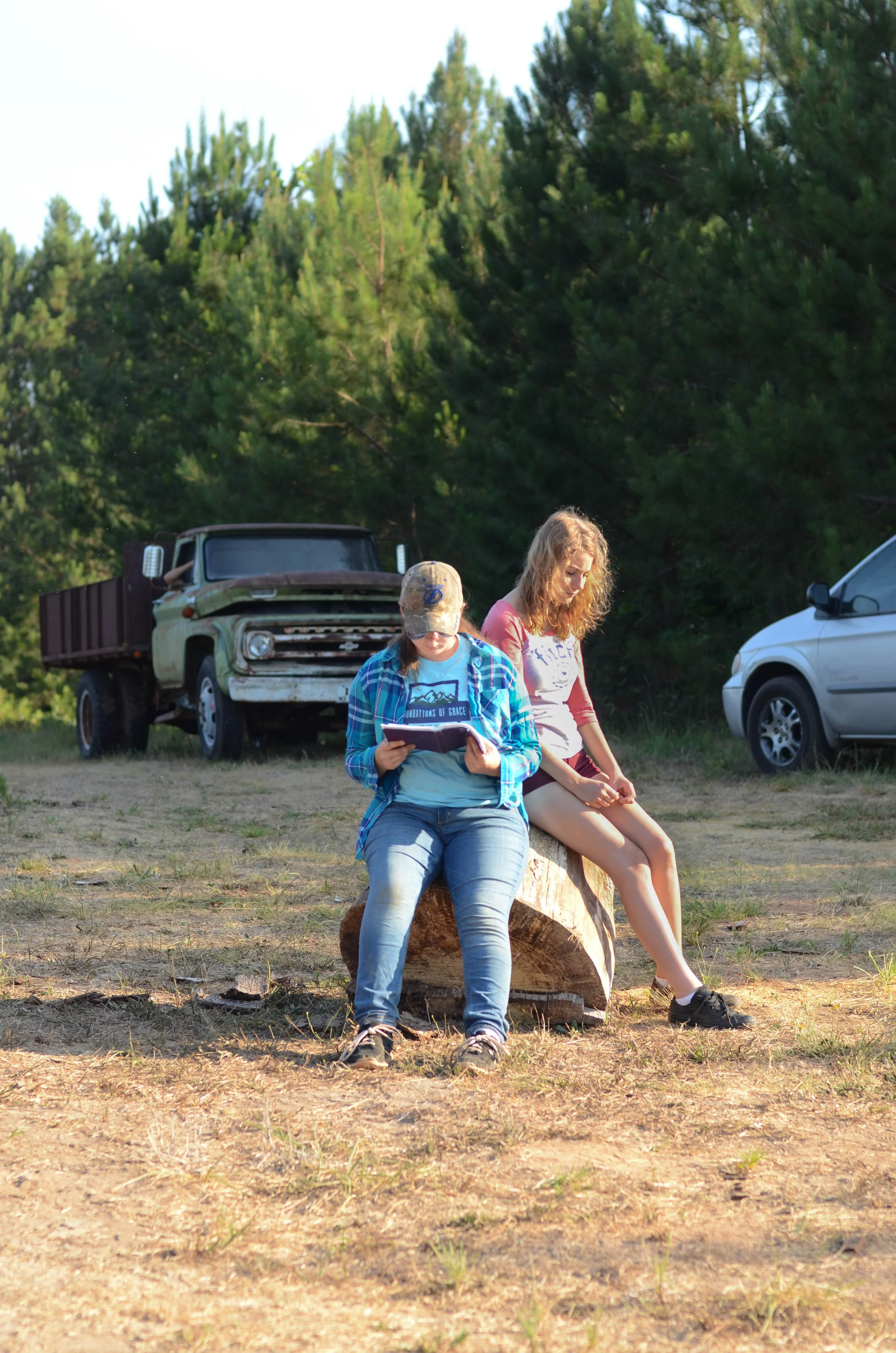 Two girls reading the bible while sitting on a tree stump