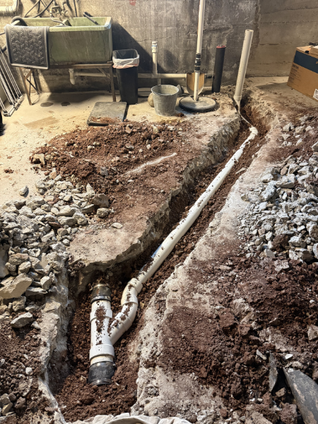 Underground plumbing installation with white PVC pipe in a construction site, surrounded by dirt and gravel.