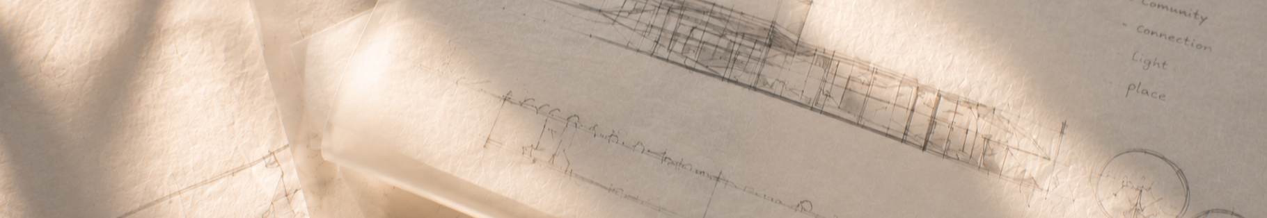 Architectural plans and sketches spread out on a desk with a warm light illuminating them.