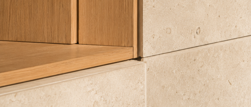 Close-up of a wall corner showing a transition between wood paneling and beige stone or tile surface.