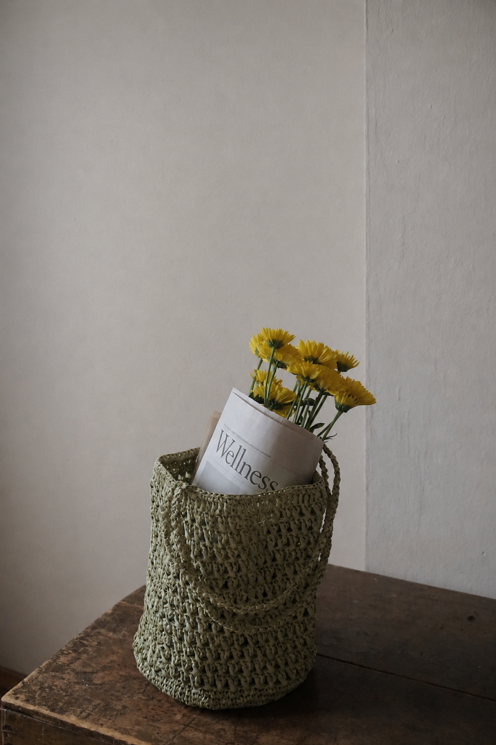 Woven green basket holding yellow flowers and a folded wellness newspaper