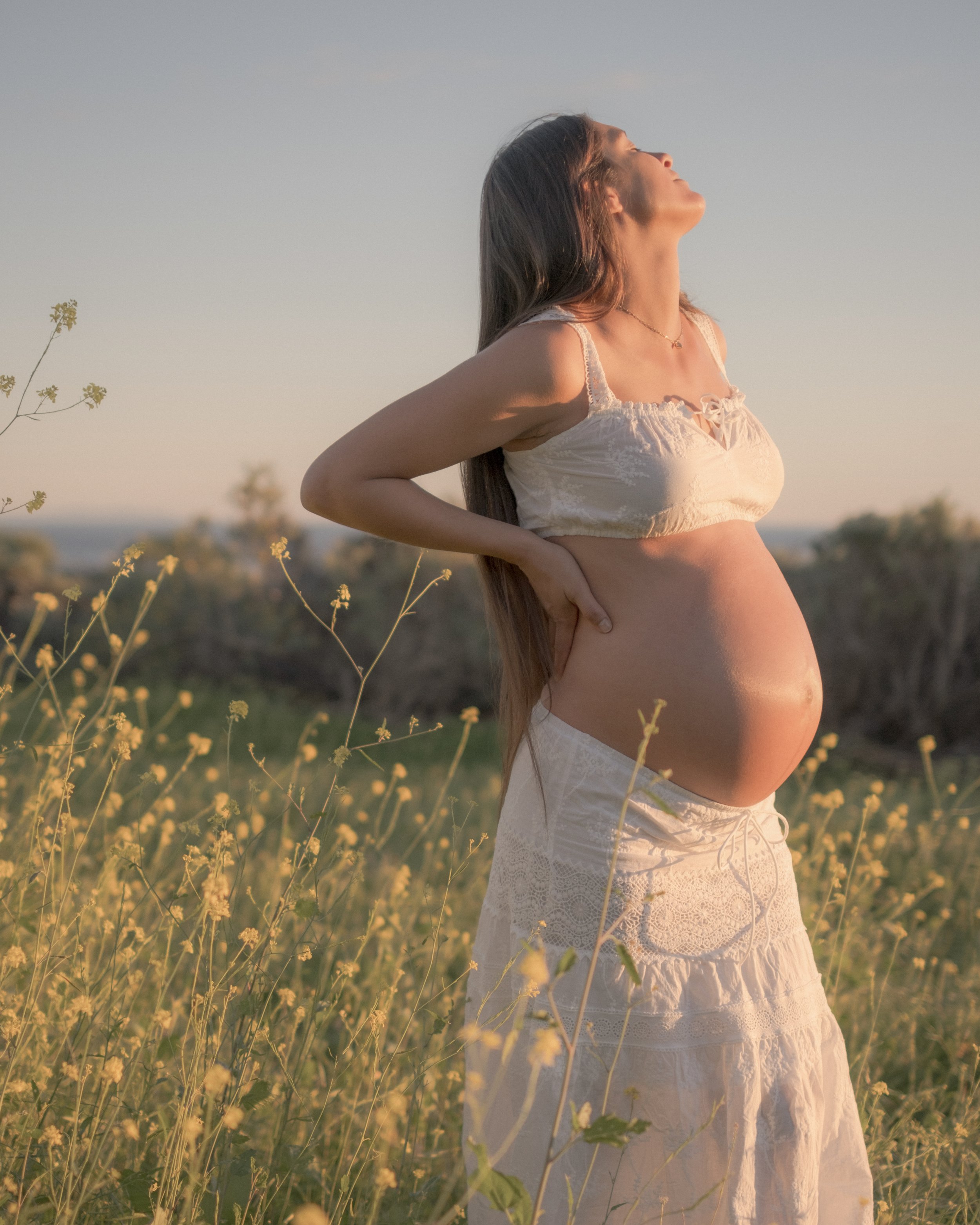 Expectant parent standing in a sunlit meadow