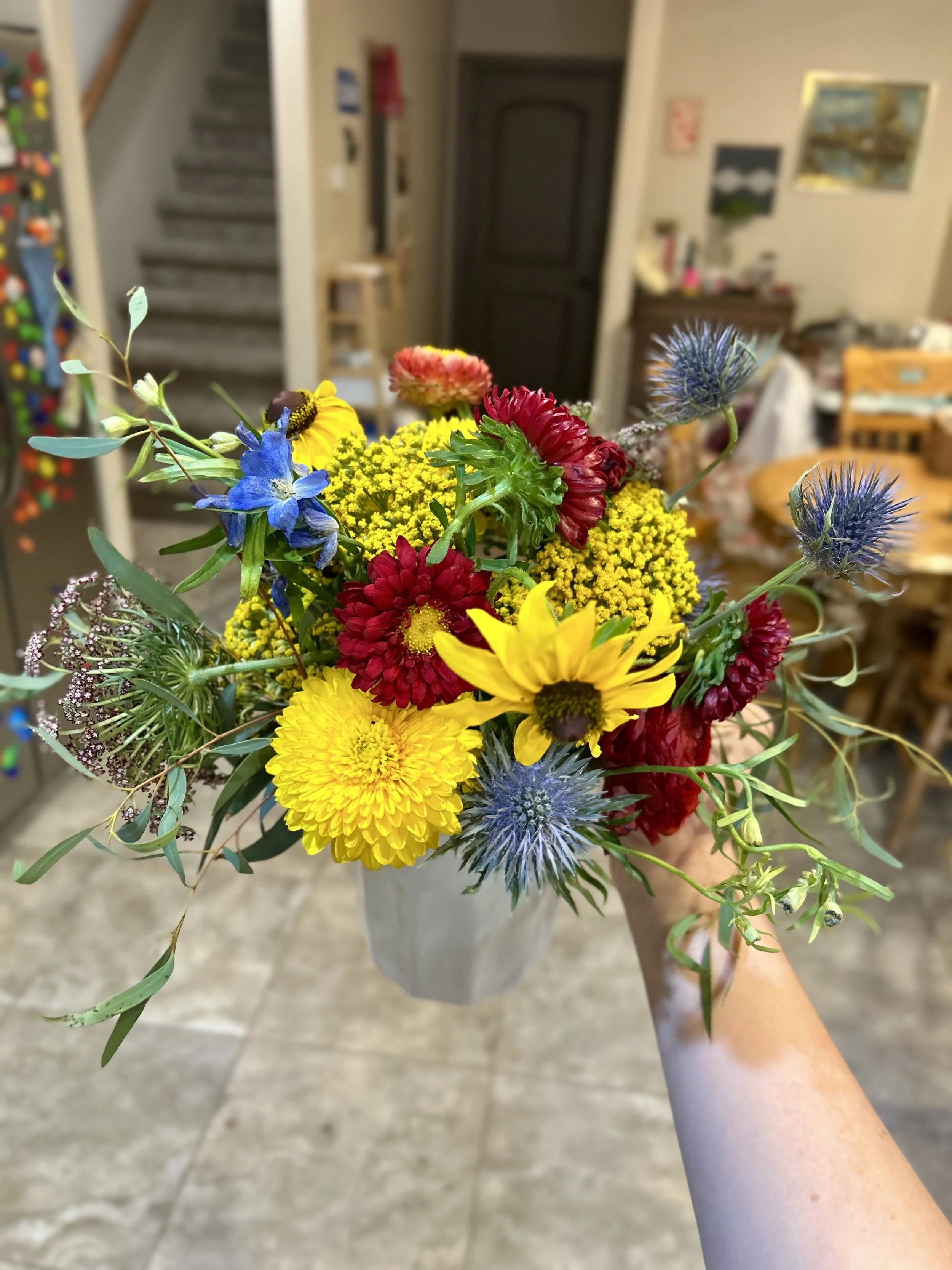 A  vibrant bouquet of mixed flowers, including yellow daisies, red chrysanthemums, blue sea holly, and other greenery.