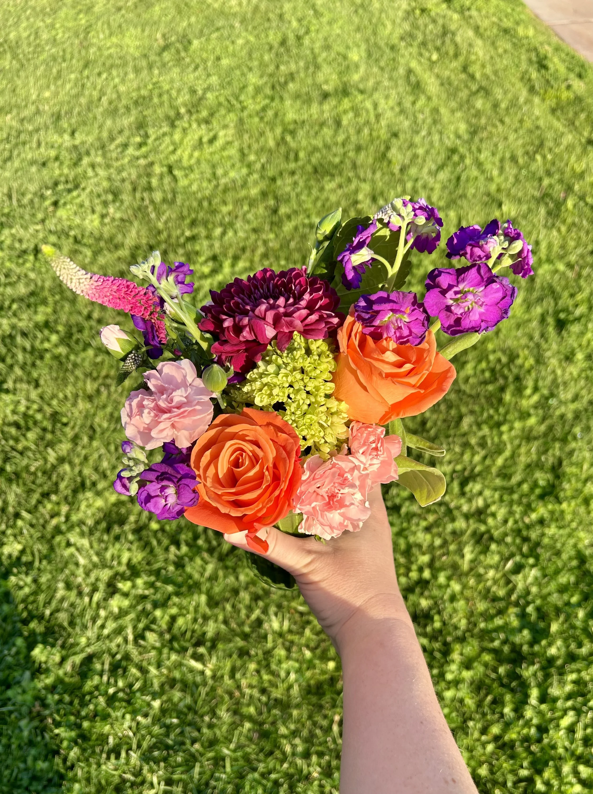 A person holding a colorful bouquet of flowers outdoors on a grassy lawn.