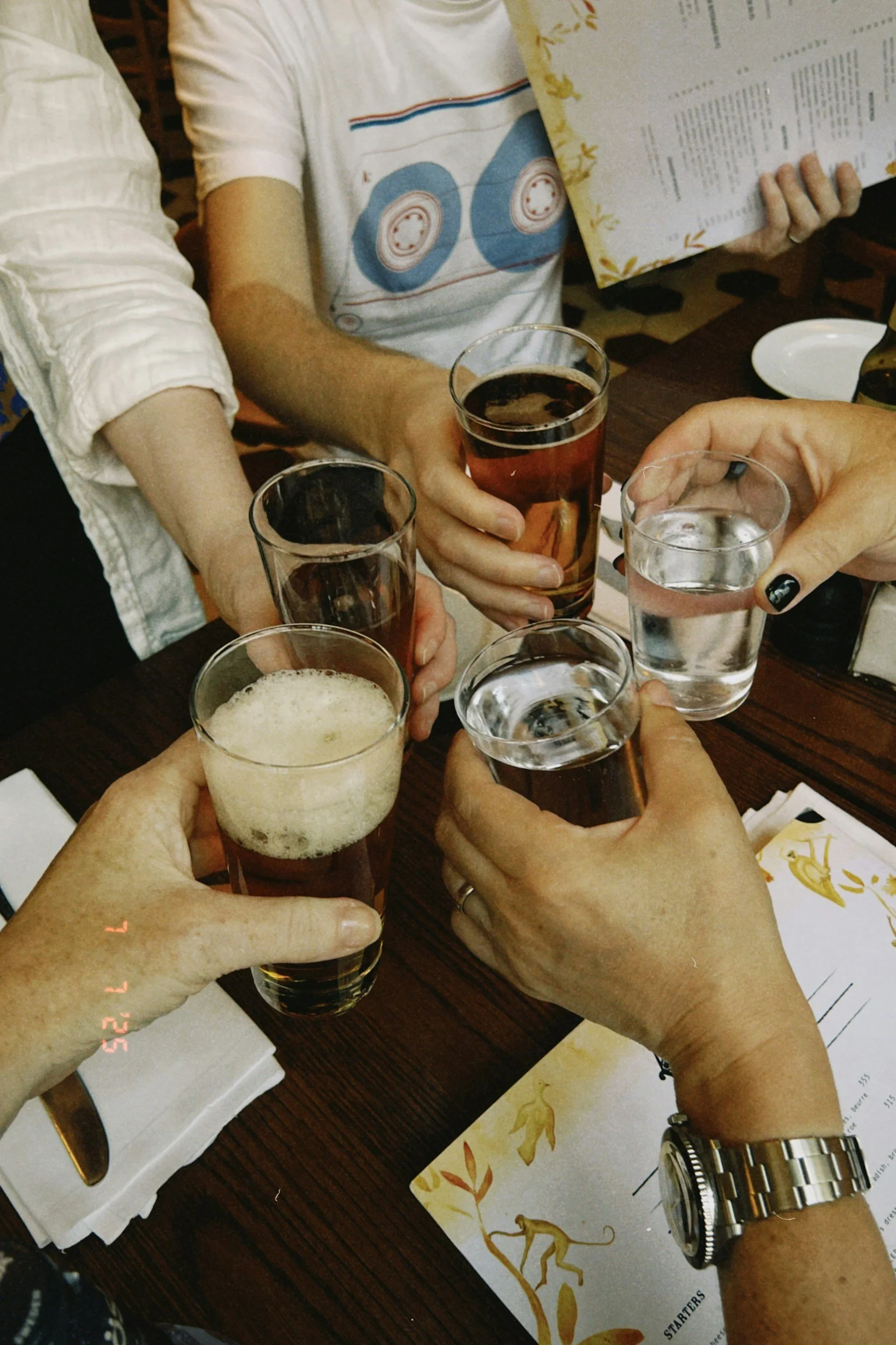People clinking glasses of beer at a restaurant table, with a menu and condiments visible.