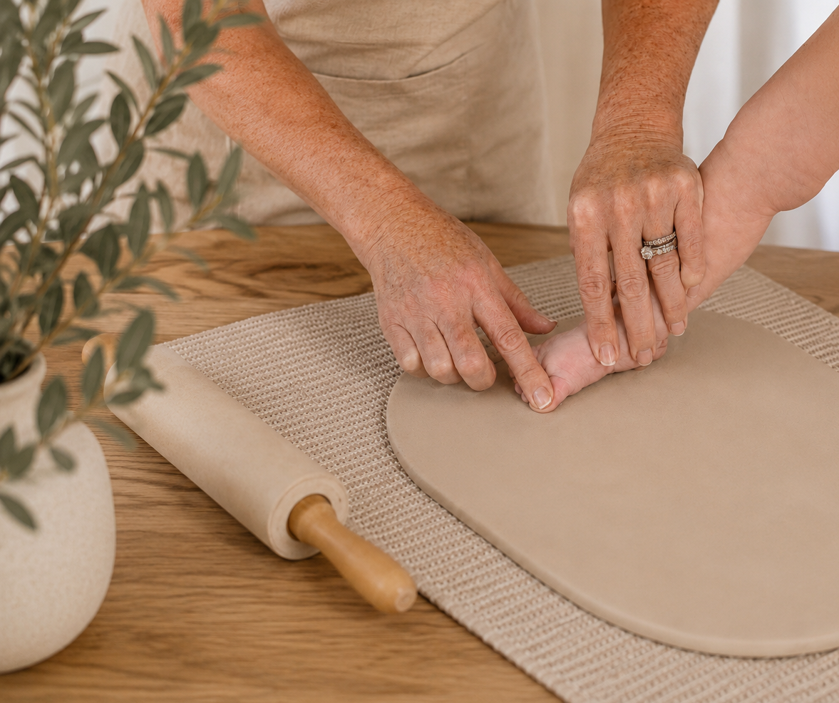 Two people making a clay heart-shaped craft on a wooden table with a rolling pin and a potted plant nearby.