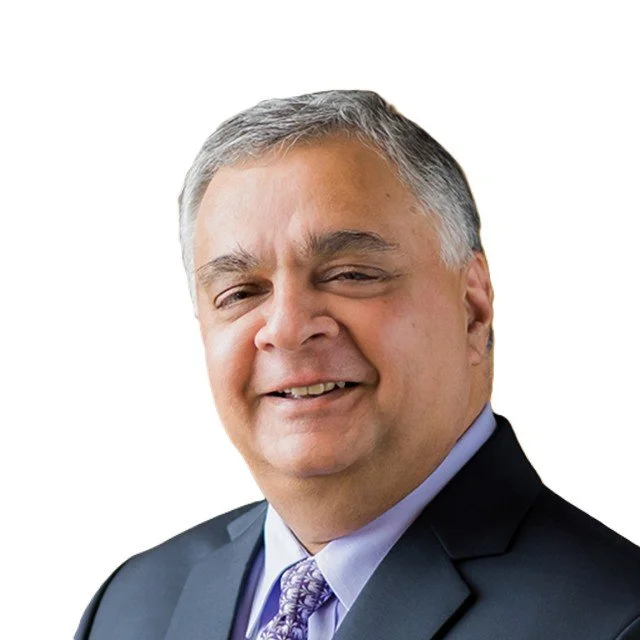 Portrait of a middle-aged man wearing a dark suit, light blue shirt, and purple patterned tie, smiling at the camera with a white background.