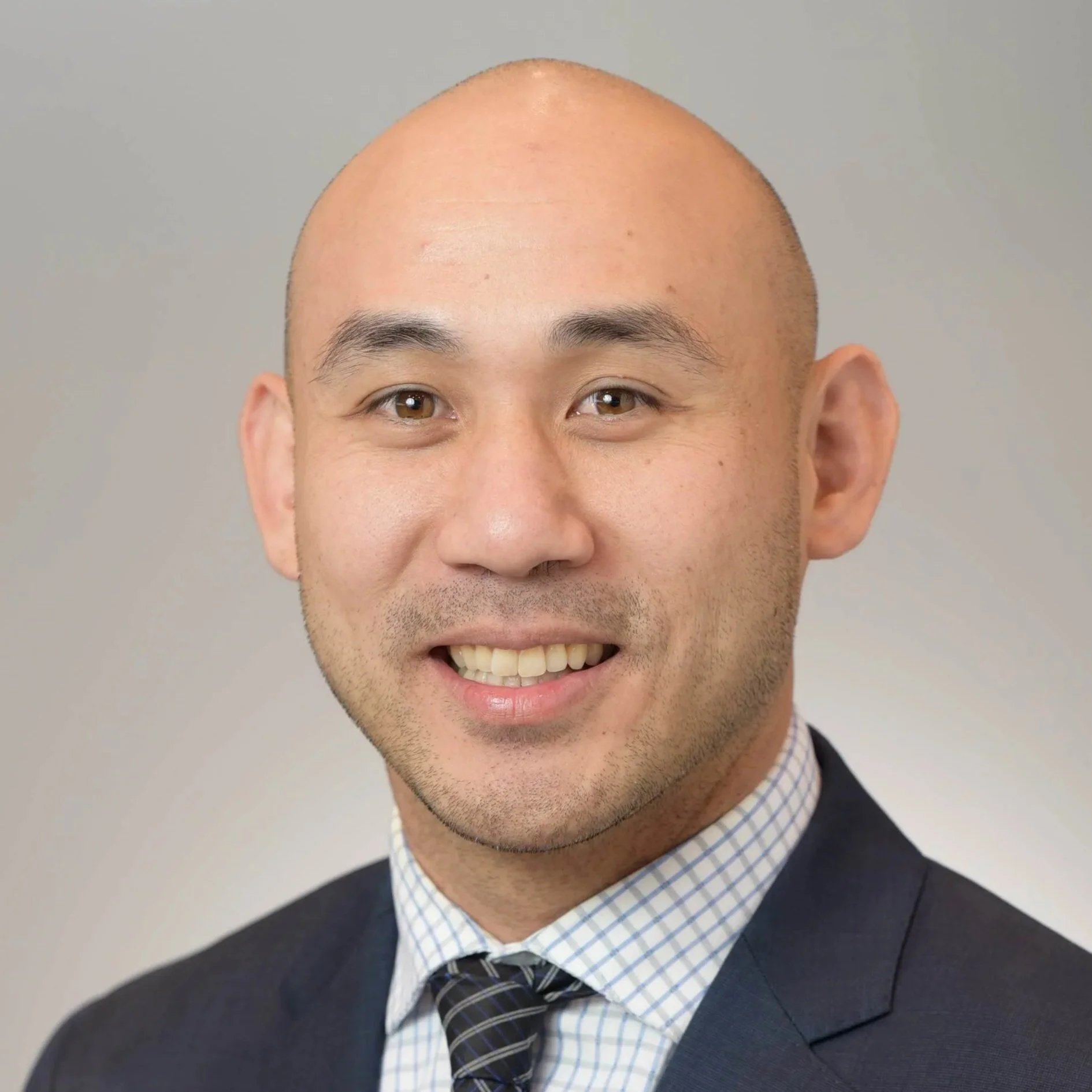 Close-up of a smiling man in business attire, with a bald head, wearing a dark blazer, a collared shirt, and a patterned tie.