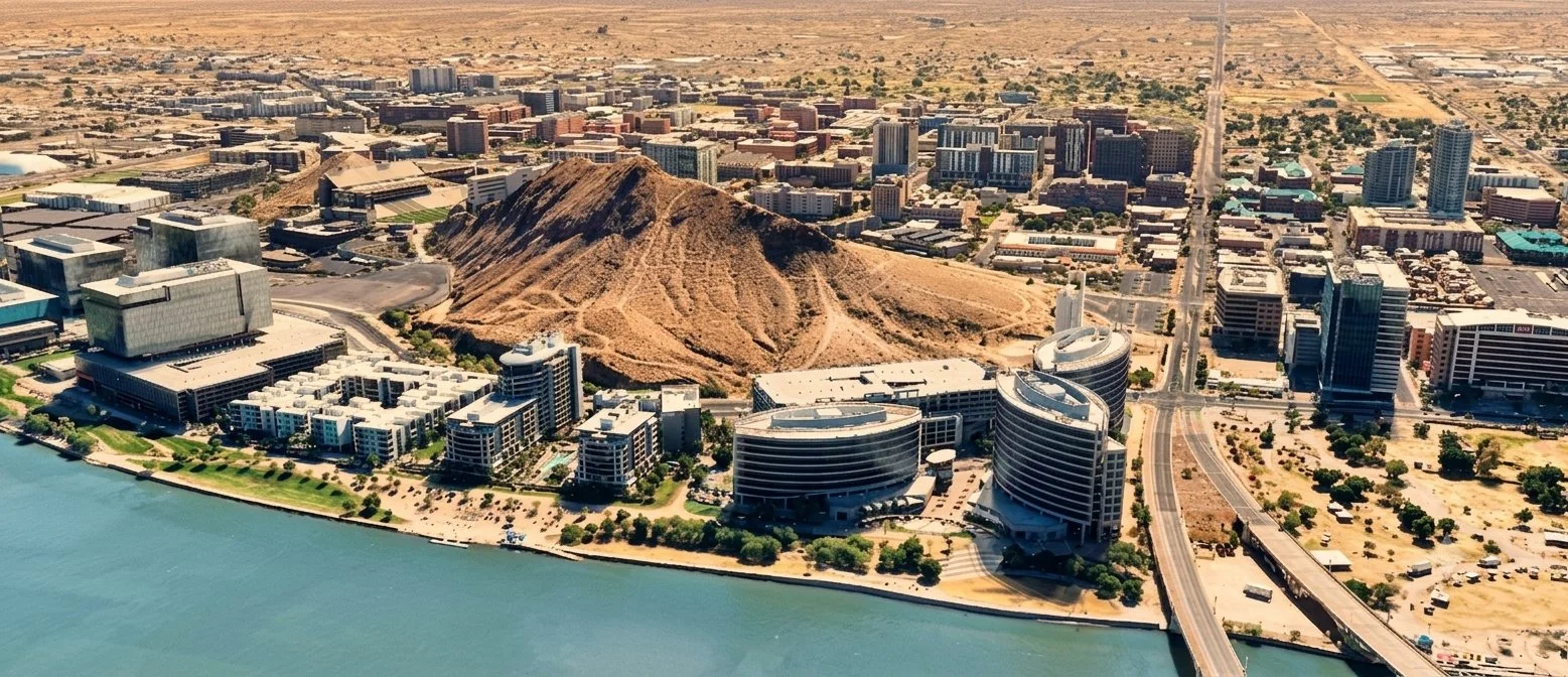 Aerial view of a city by a lake with modern buildings, a distinctive hill, and a mix of high-rise and low-rise structures.