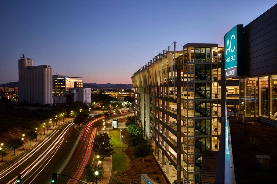 Night view of AC Hotels by Marriott with illuminated building and street with light trails from moving vehicles in an urban area at dusk.
