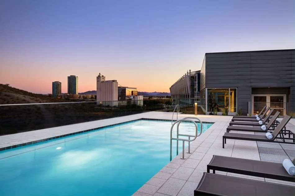 Rooftop swimming pool area with lounge chairs and a cityscape at sunset.