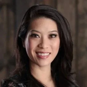A portrait of a woman with dark hair, smiling, against a wooden background.