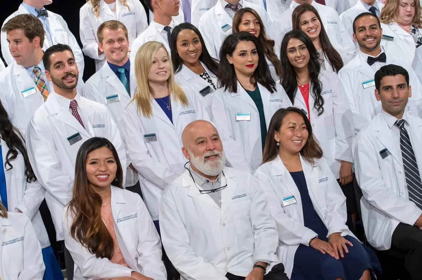 Group of diverse medical students and a professor in white coats attending a graduation or educational event.