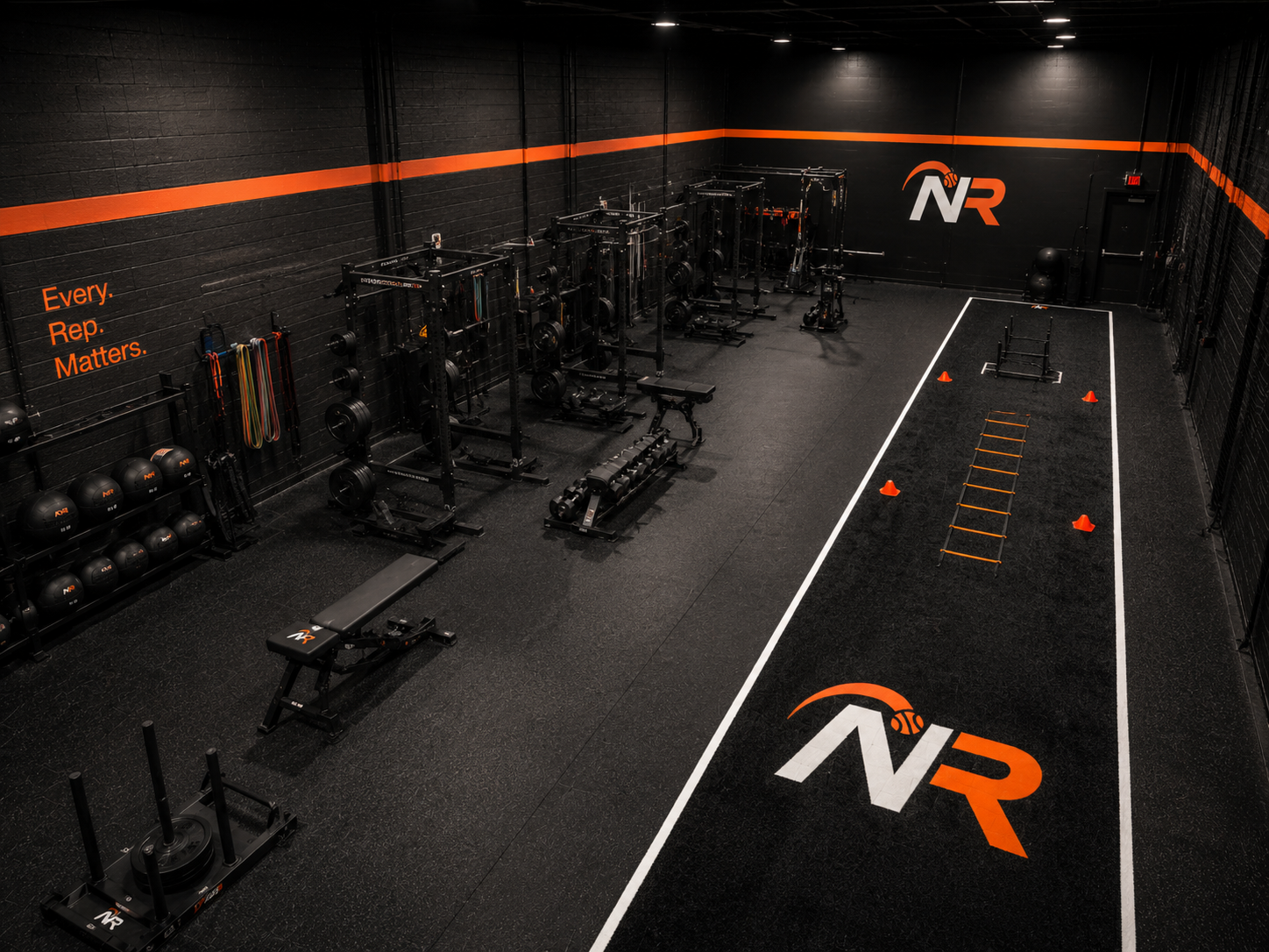 Empty indoor gym with black walls, orange accents, and workout equipment including weights, resistance bands, a bench, medicine balls, agility ladder, cones, and a sled on a marked court with the NR logo.